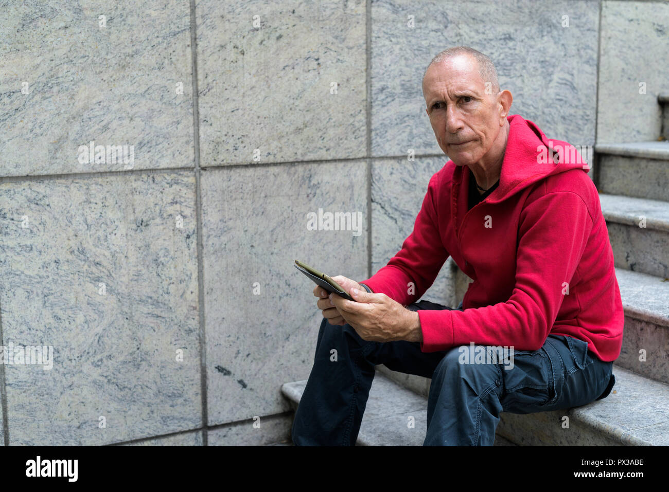 Kahlen älterer Mann denken und halten digitale Tablet während sittin Stockfoto
