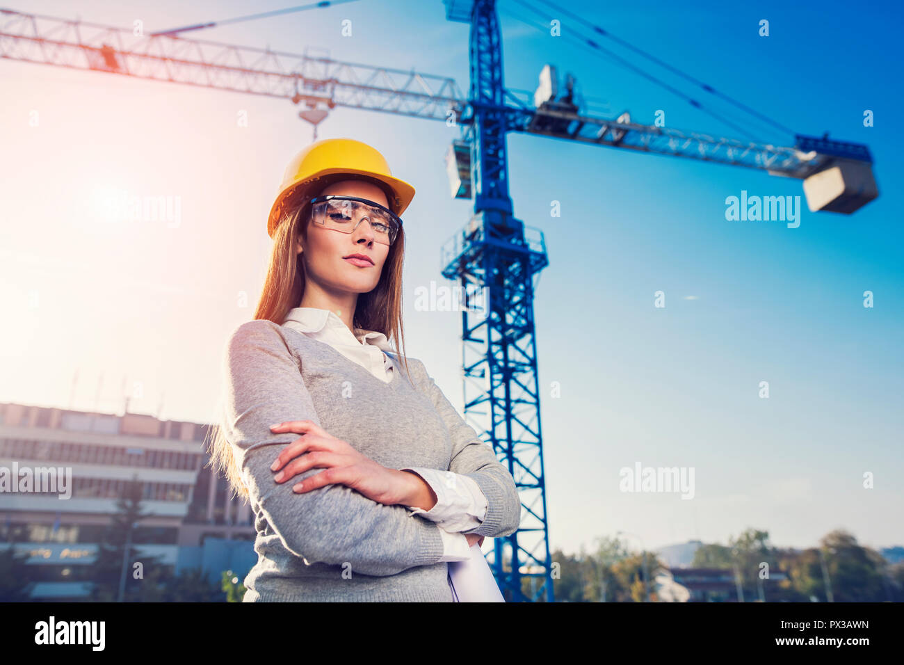 Schöne Frau Bauingenieur lächelnd mit Zuversicht vor einem Kran in einem Sonnenuntergang flare Hintergrund Stockfoto