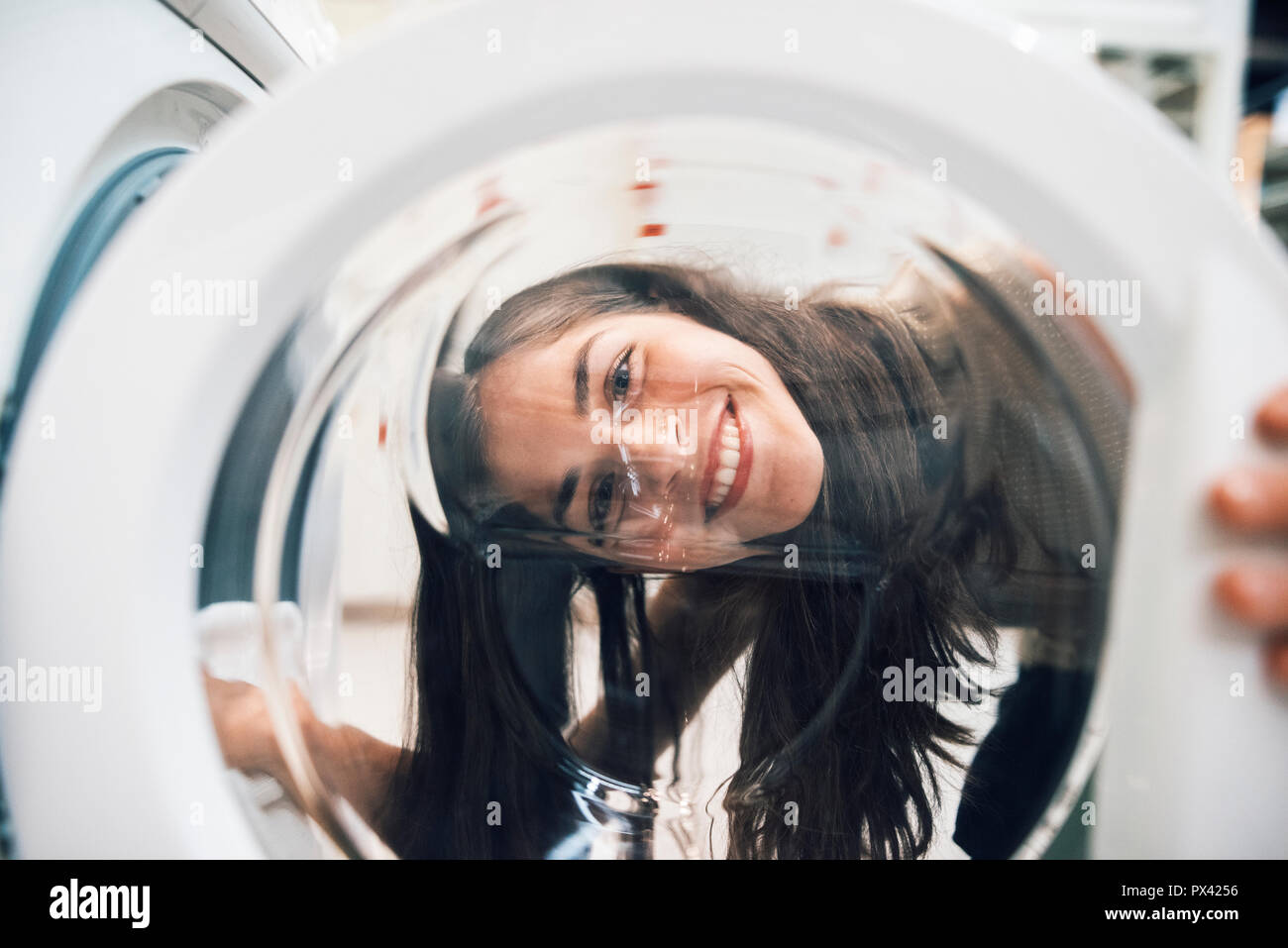 Frau fröhlich lächelnd durch eine Waschmaschine Tür Stockfoto