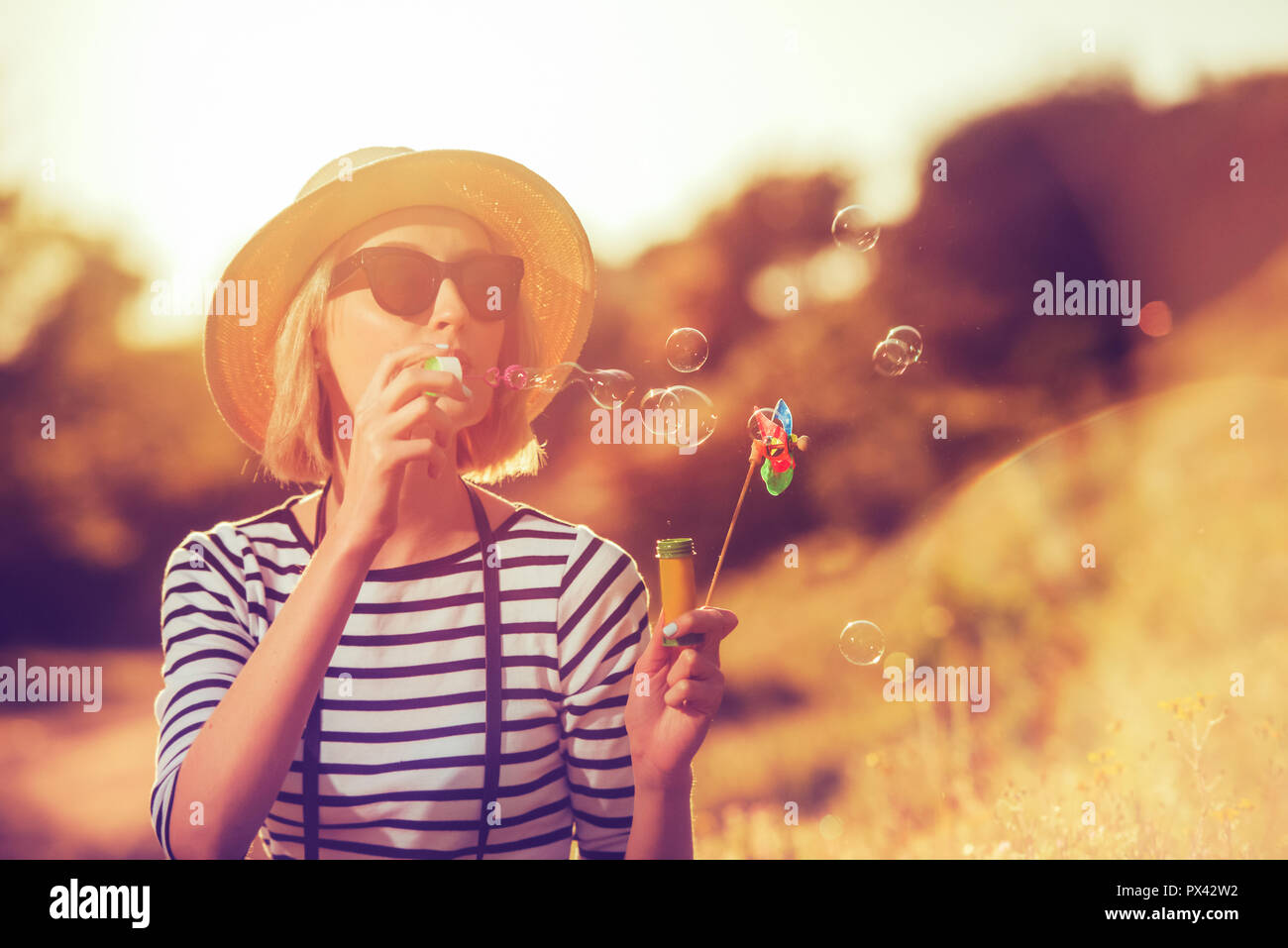 Eine schöne junge Frau touristische bläst Seifenblasen mit einem windmil Spielzeug auf ein Sonnenuntergang Hintergrund Stockfoto