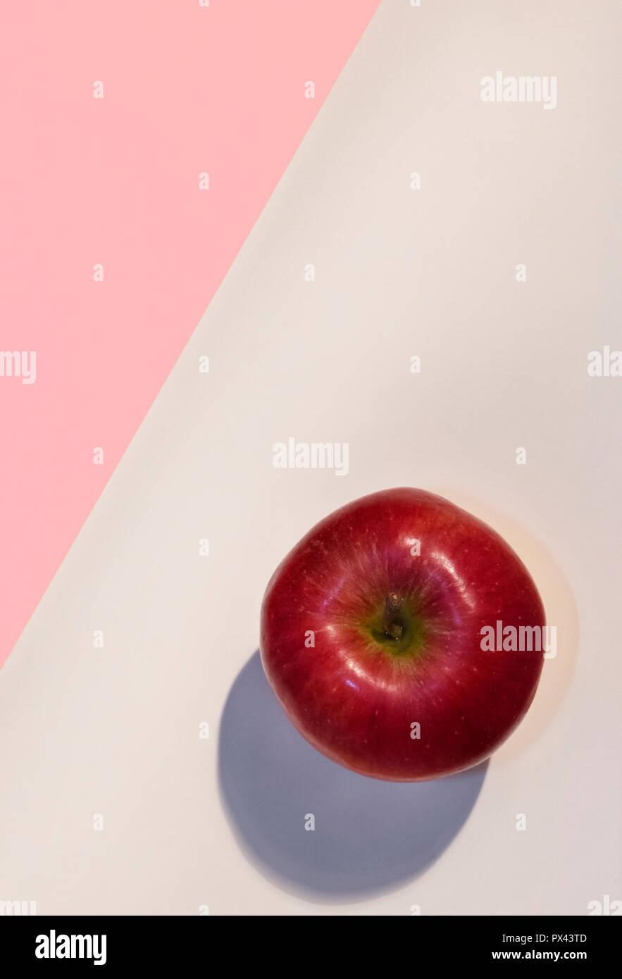 Ein heller roter Apfel auf einem rosa und weißen Hintergrund, schöne Farben, studio Shot, Ansicht von oben, vertikale Zusammensetzung Stockfoto