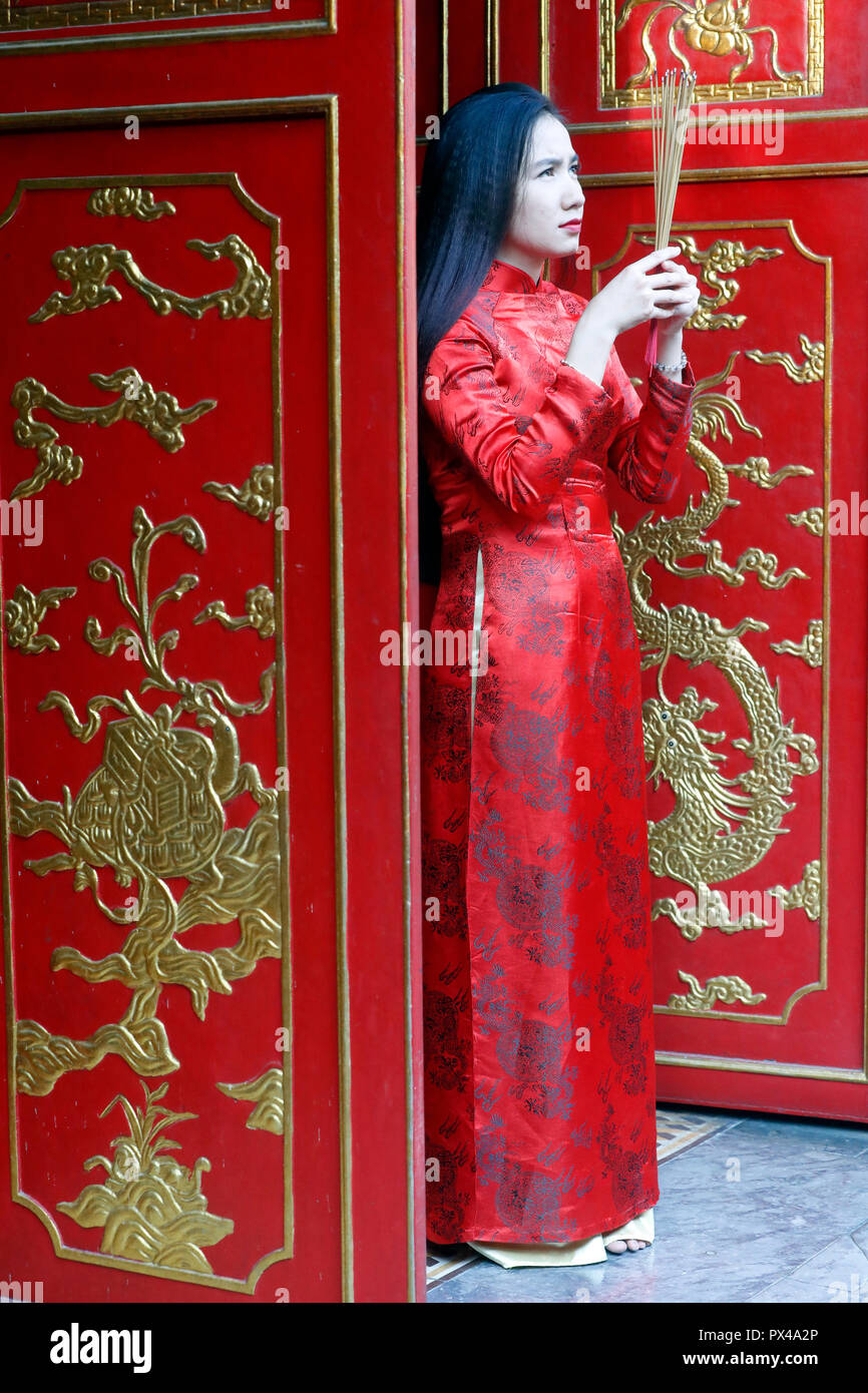 Vietnamesische Frau in Rot traditionelle langes Kleid Ao Dai beten mit Räucherstäbchen. Ho Chi Minh City. Vietnam. Stockfoto