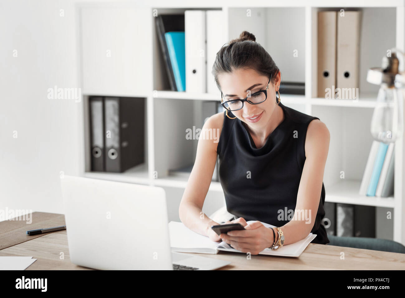 Eine junge Frau Manager prüfen Ihr Telefon in Ihrer Workstation. Über Office Arbeit, Technik kommunizieren, Smart Phones, Anwendungen, Arbeiten, Zeitplan Stockfoto