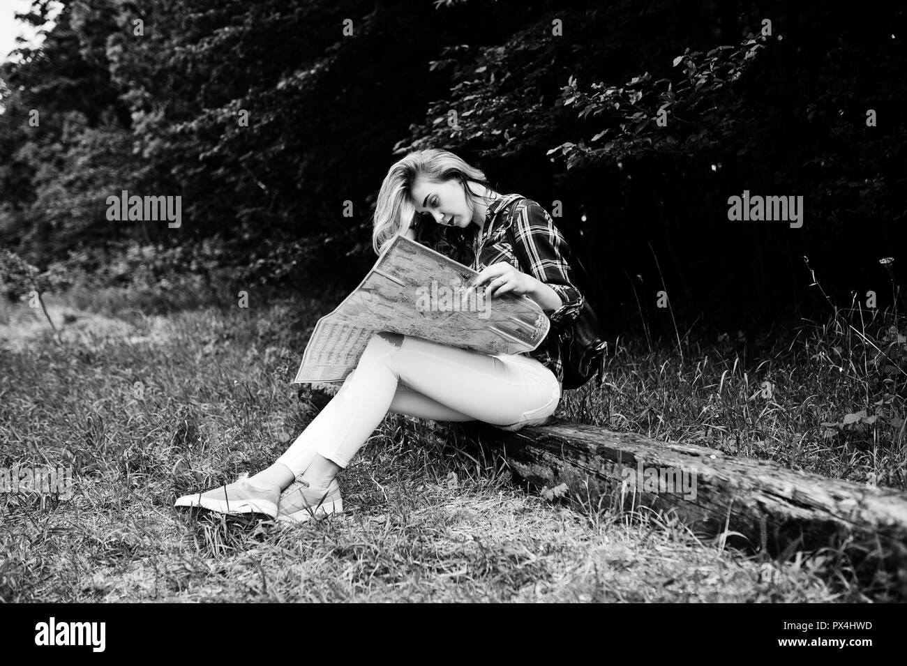 Porträt einer positiven junge wunderschöne Blondine auf dem Boden sitzend mit einer Karte in den Händen in den Wald. Stockfoto