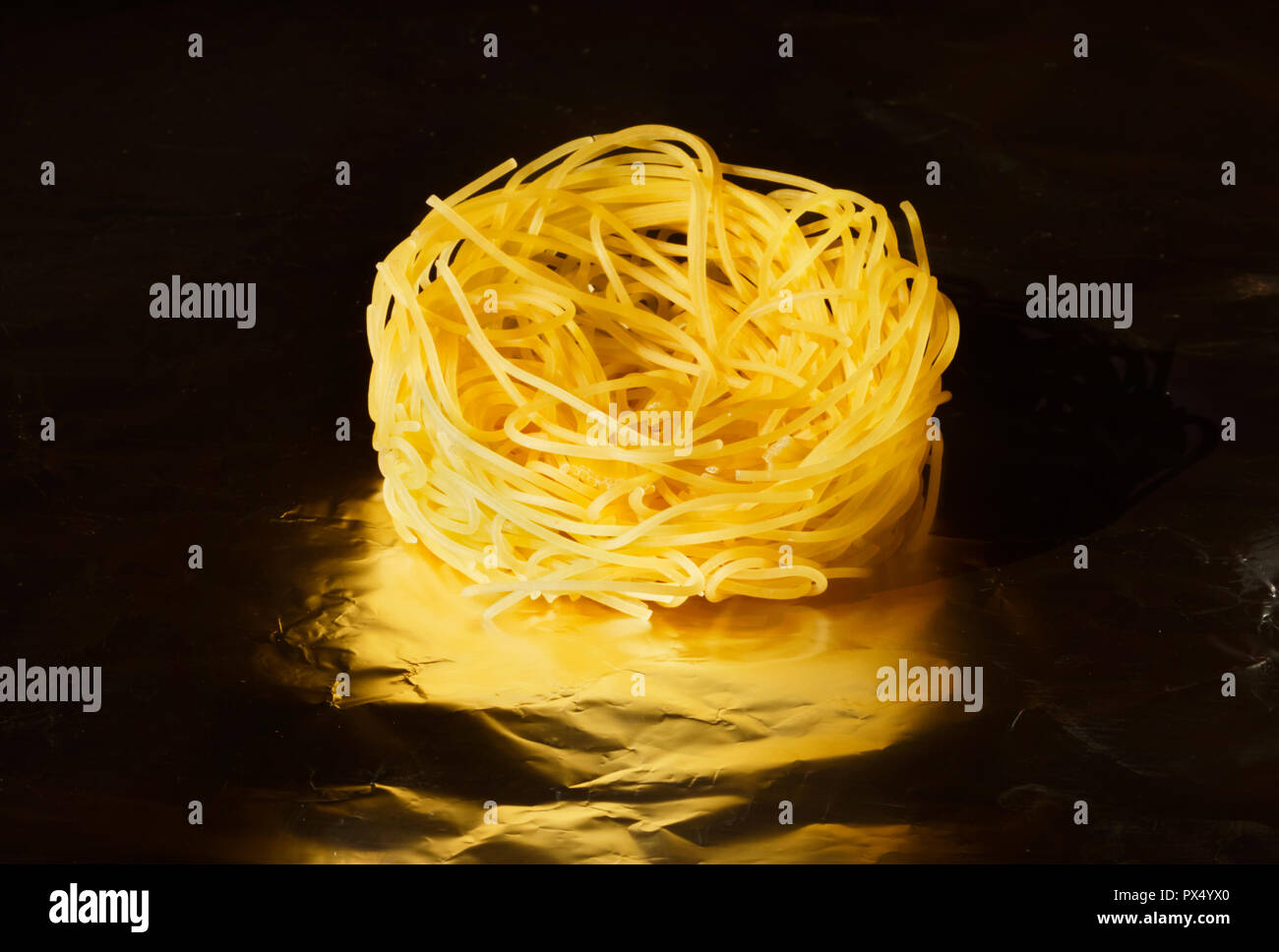 Trockene und dünne Bänder von trockenteigwaren namens Angel hair Pasta, ein helles Nest auf einem dunklen Hintergrund aus Aluminiumfolie, studio Shot, Ansicht von oben Stockfoto