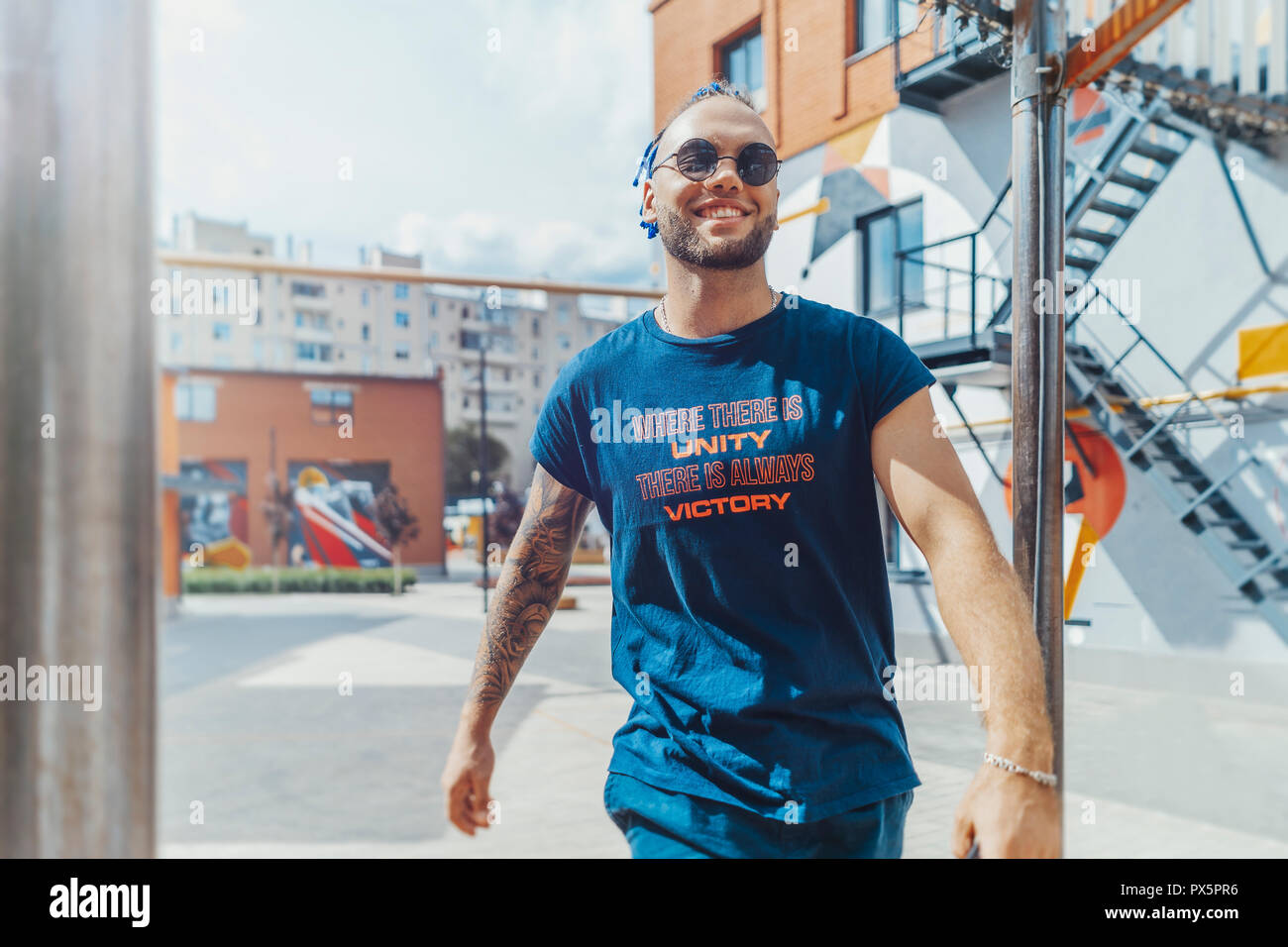 Mann mit blauen Dreadlocks neben dem roten gemauerte Gebäude geht. Stockfoto