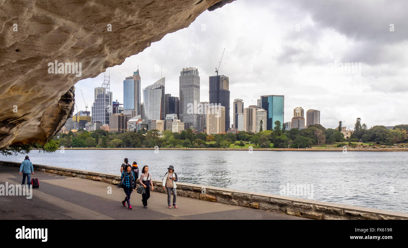 Fußgänger auf dem Weg entlang Farm Cove Sydney Harbour mit Bürogebäude und CBD Skyline an einem bewölkten Tag Sydney, NSW, Australien. Stockfoto