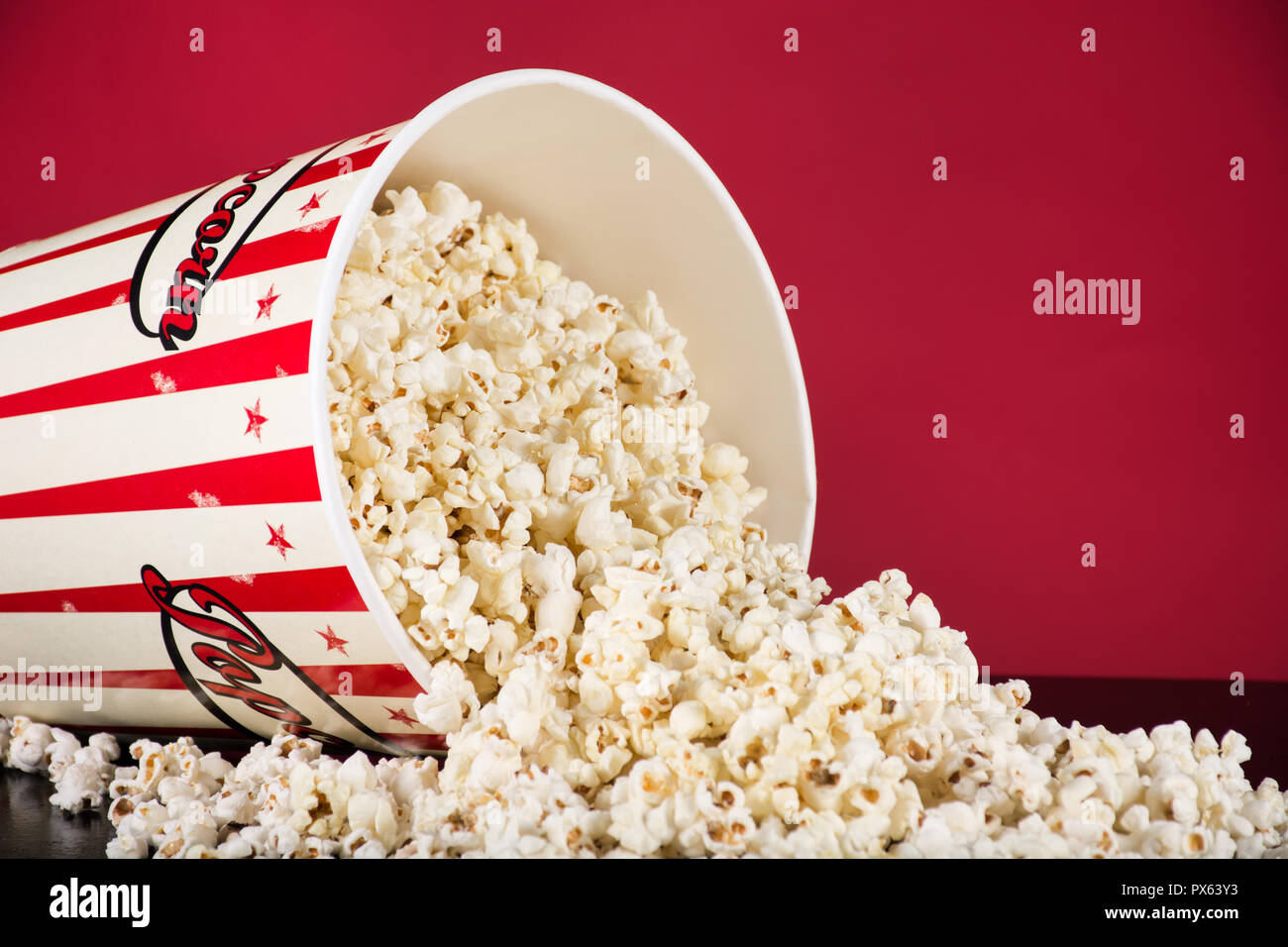 Verschütteten popcorn Box auf schwarzen und roten Hintergrund. Retro weiß und rot. Kino und Film food Konzept. Close Up, selektiver Fokus Stockfoto