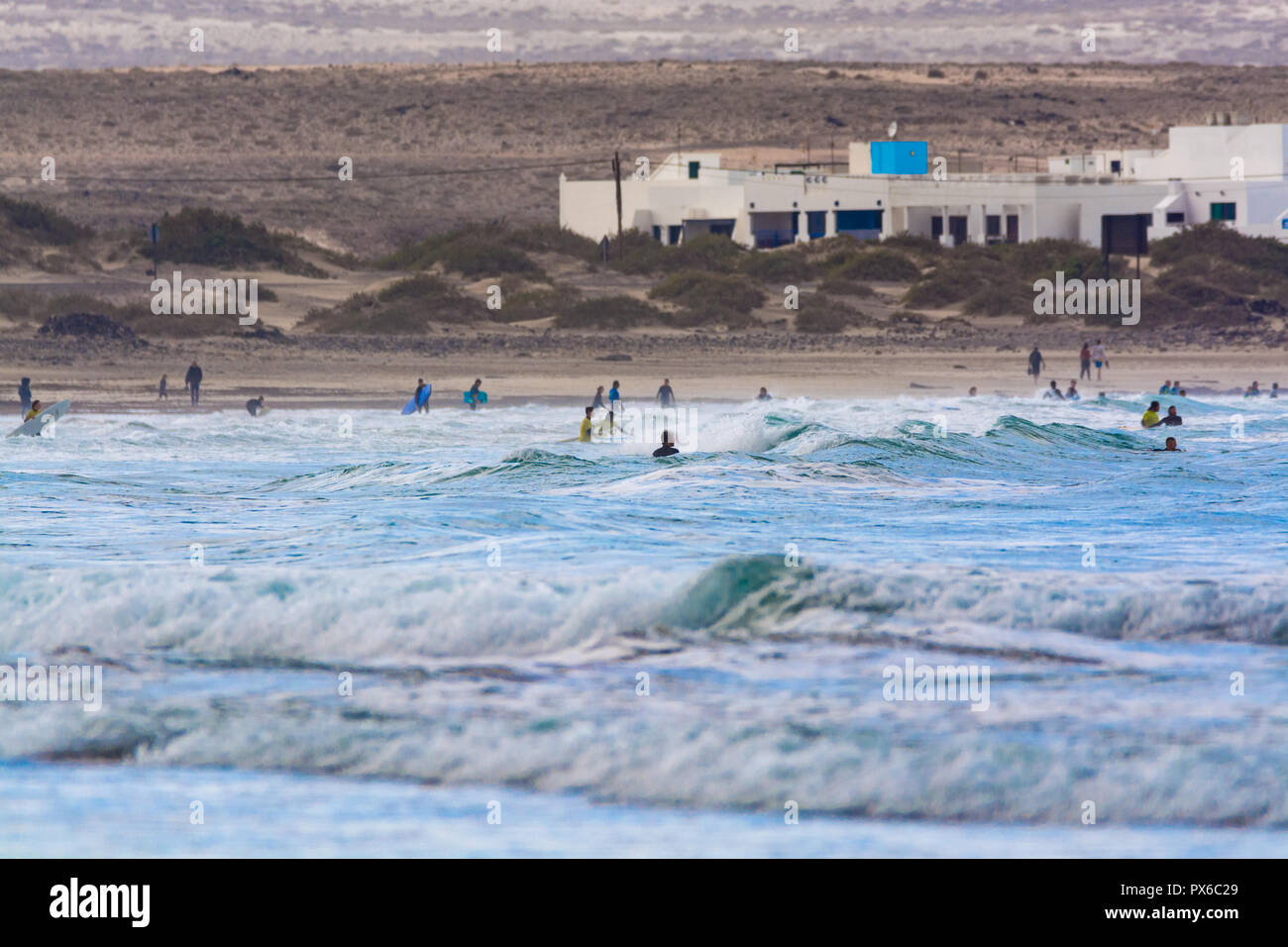 Undefinierte Surfer mit Surfbrett im Wasser des Atlantischen Ozeans, Winter auf der Insel Lanzarote, Famara Strand, berühmten Ziel für Surfer Stockfoto