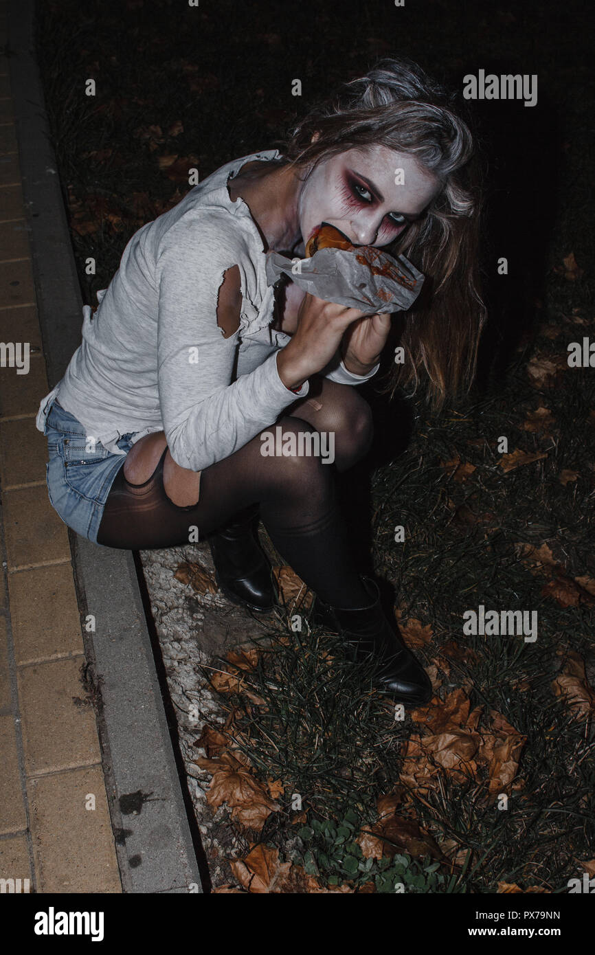 Das Mädchen auf dem Bild von einem Zombie mit einem weißen Gesicht in einer  zerrissenen t-shirt, denim Shorts und schwarzen Strumpfhosen sitzt auf dem  Bürgersteig und einen Burger essen Stockfotografie - Alamy