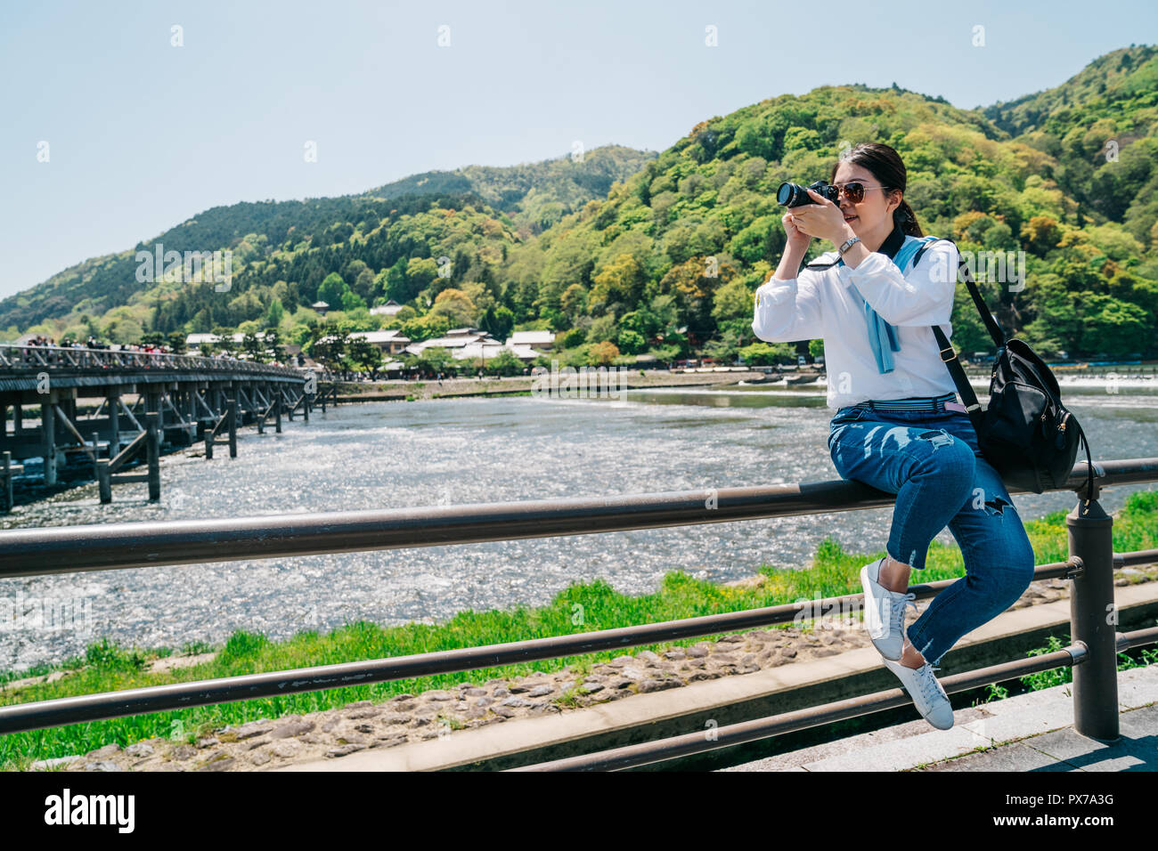 Elegante Fotograf Sitzen auf dem Geländer und Bild der Togetsukyo Brücke. Reisen objektiv Mann Hobby liebe Landschaft Foto von SLR-ca Stockfoto