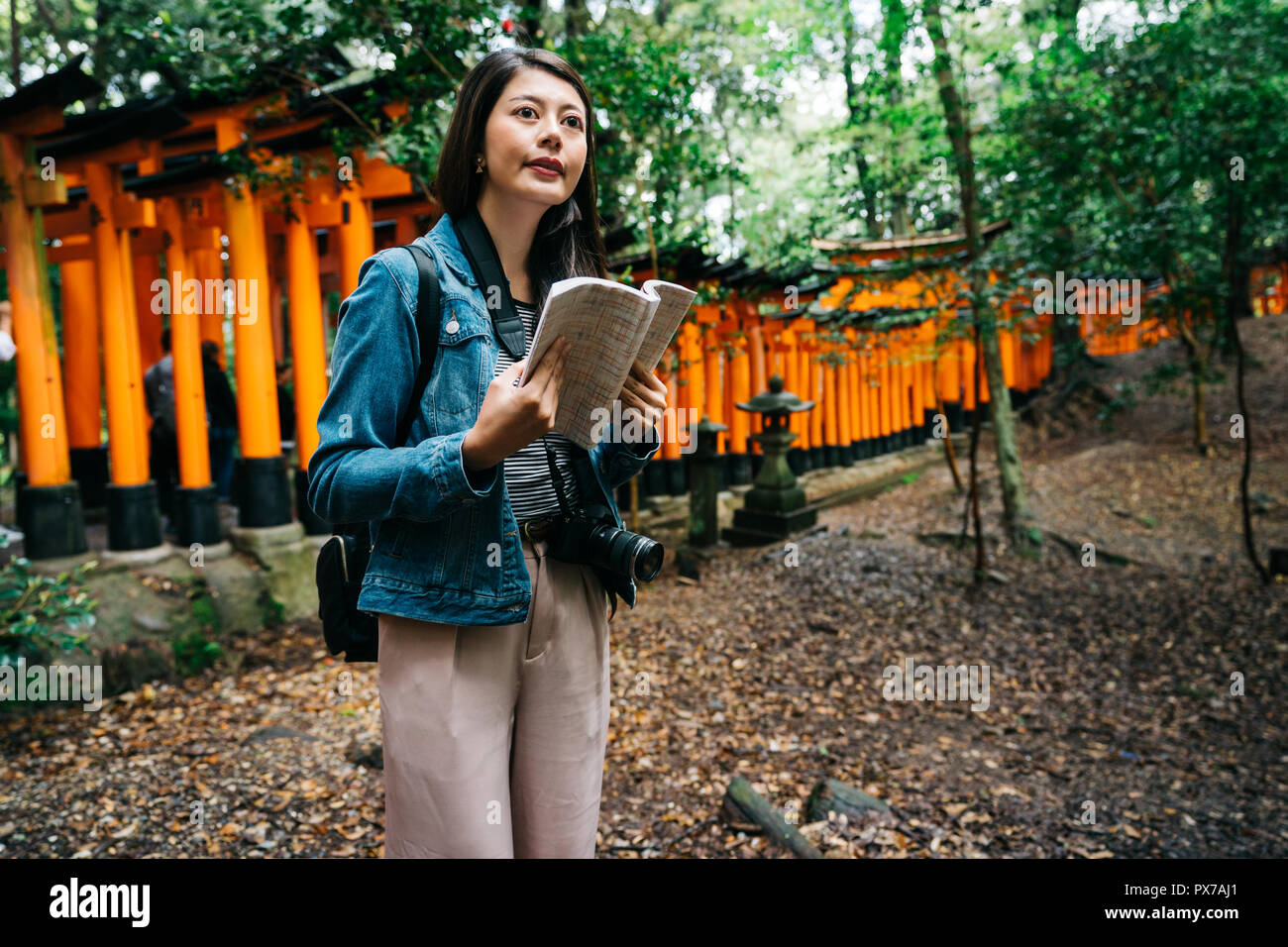 Elegante asiatischen Fotografen stehen in der Nähe des Torii und ihre Ratgeber Holding. Weibliche objektiv Mann im grünen Wald in Kyoto. Japan Reiseziel im Sommer. Stockfoto