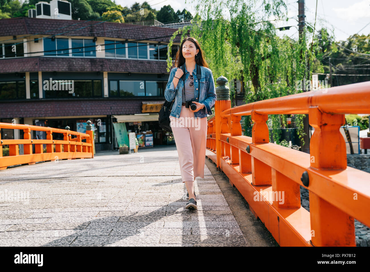 Volle Länge Foto eines eleganten asiatischen Reisenden zu Fuß auf die Brücke mit einem attraktiven Lächeln auf ihrem Gesicht. Berühmte Sehenswürdigkeiten in Kyoto Uji Brücke. kop Stockfoto