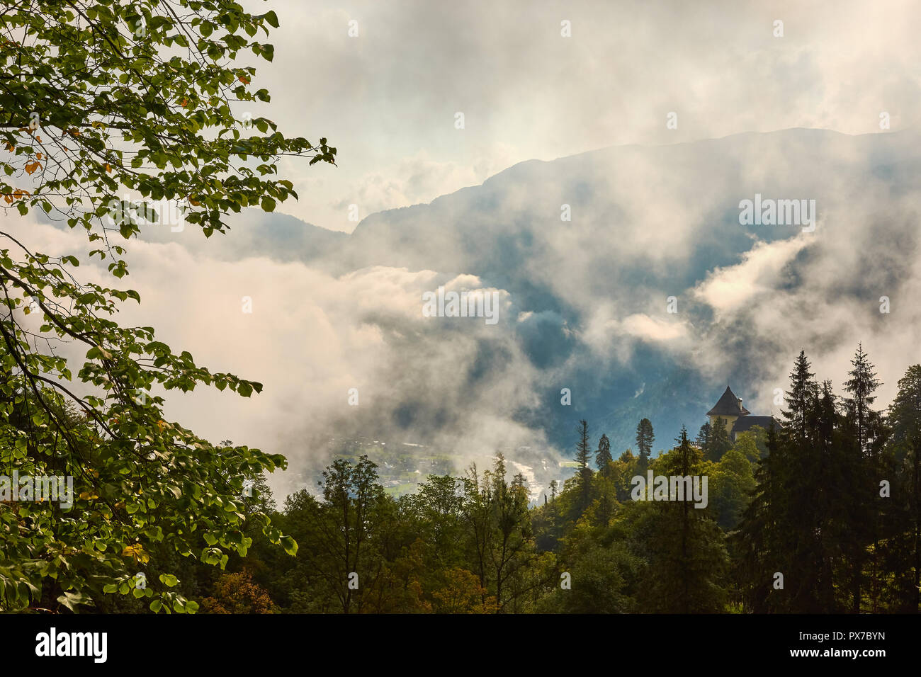 Wald auf einem Hügel zwischen den Bergen über Hallstatt in Österreich, mit Wolken, Nebel und Himmel Hintergrund Stockfoto