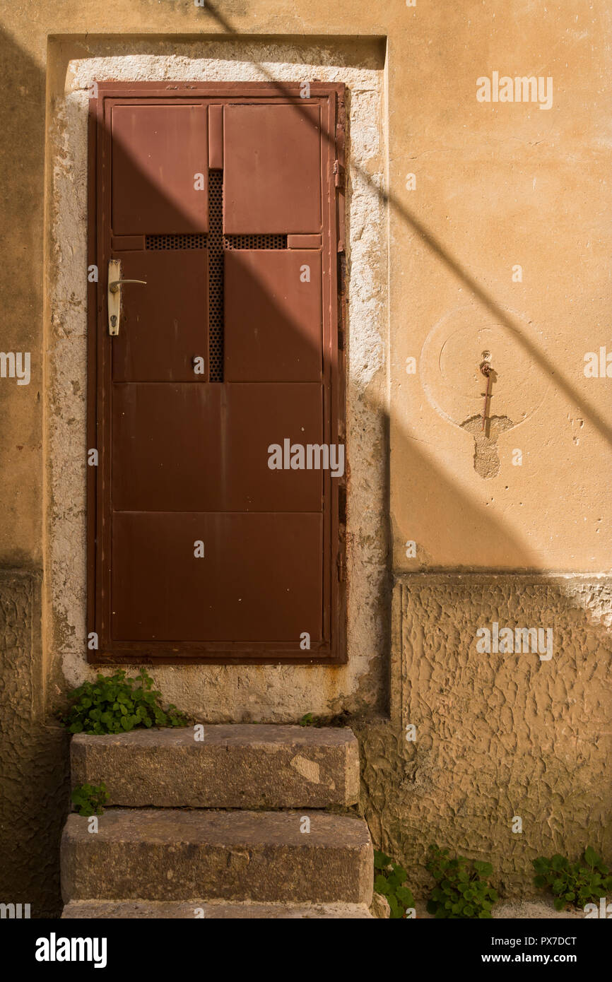 Braun Bügeleisen Tür mit einem Kreuz und einem goldenen Griff. Shadow Line über das Bild. Steinerne Treppen. Gelbe Fassade. Historische Stadt Vrbnik, Krk, Cro Stockfoto