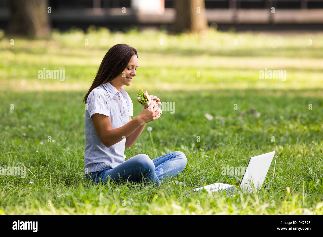 Schöne Geschäftsfrau ruht sich aus Arbeit, essen Sandwich und mit Laptop. Stockfoto