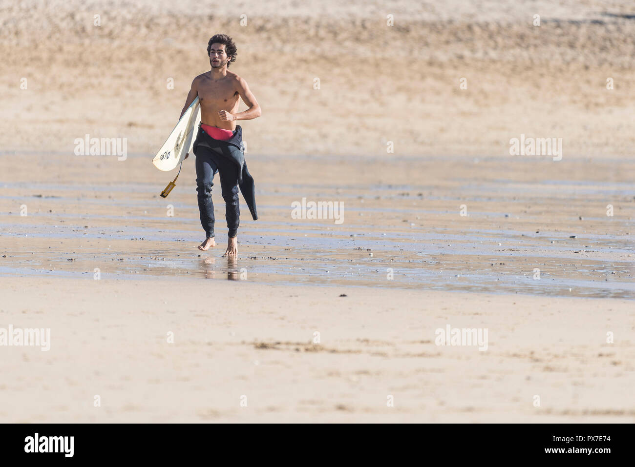 Ein Surfer sein Surfbrett tragen und entlang den Fistral Beach zum Meer. Stockfoto