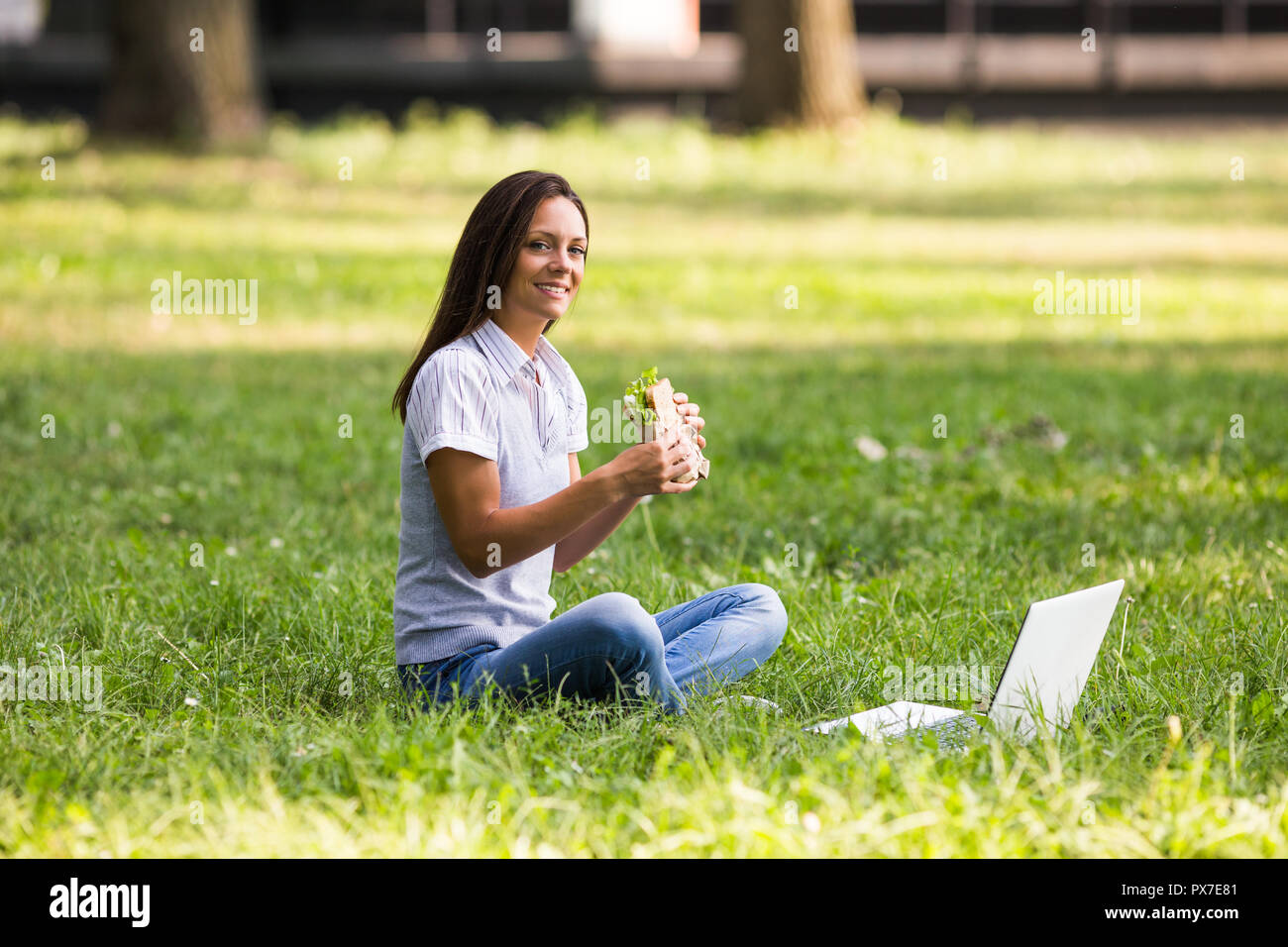 Schöne Geschäftsfrau ruht sich aus Arbeit, essen Sandwich und mit Laptop. Stockfoto