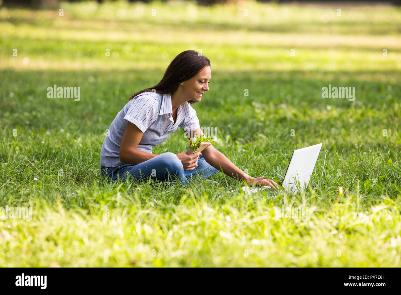 Schöne Geschäftsfrau ruht sich aus Arbeit, essen Sandwich und mit Laptop. Stockfoto