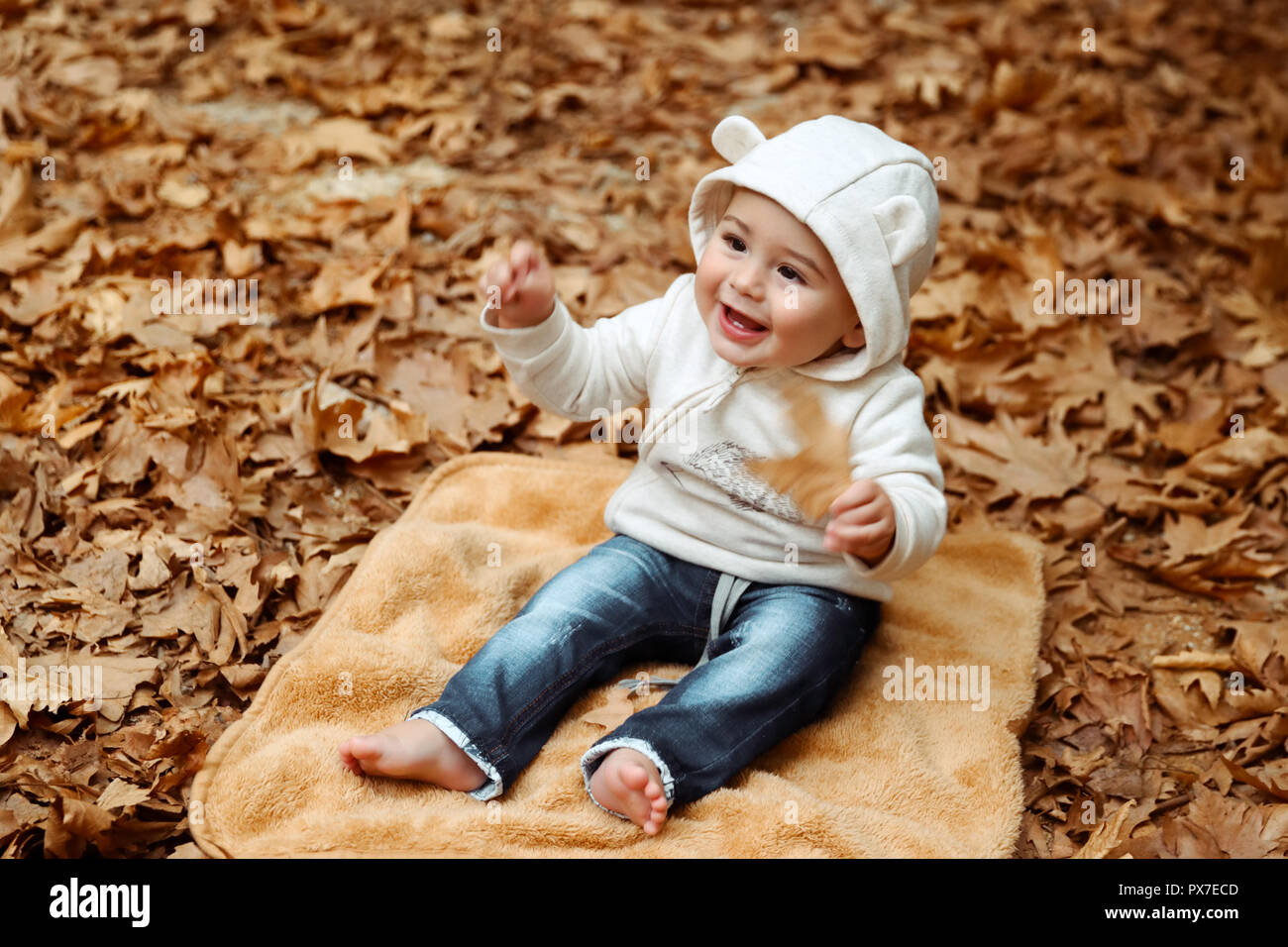 Fröhliche Junge mit Vergnügen die Zeit im Herbst Park, Little Baby sitting barfuß auf die Decke auf dem Boden mit trockenen Baum Blättern bedeckt, h Stockfoto