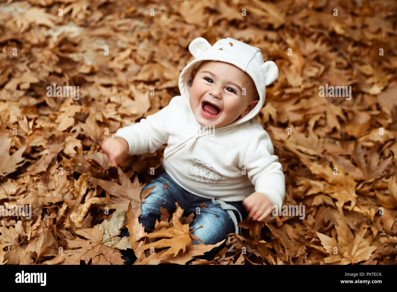 Süße kleine Junge im Stapel der trockenen Baum Blätter sitzen und Lachen, genießen die schöne und warme Wetter der Herbst Stockfoto