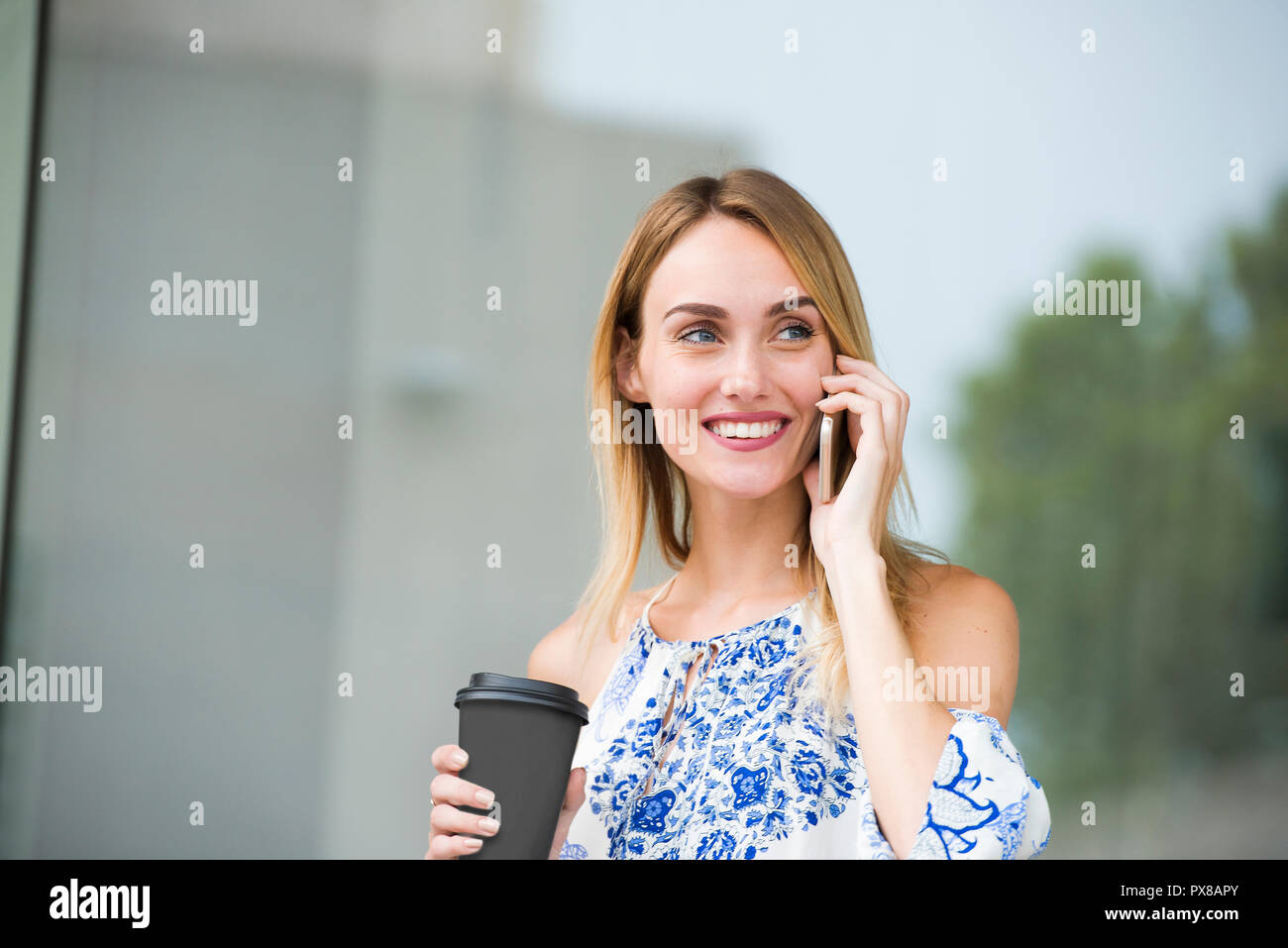 Schöne junge Frau fühlt sich glücklich, während sie zum Telefon und Halten einer Tasse Kaffee Stockfoto
