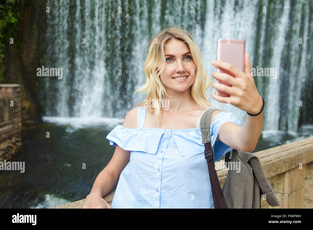 Schöne blonde Mädchen machen selfie auf dem Hintergrund eines Wasserfalls. Sie reist und Spaß haben Platz kopieren Stockfoto