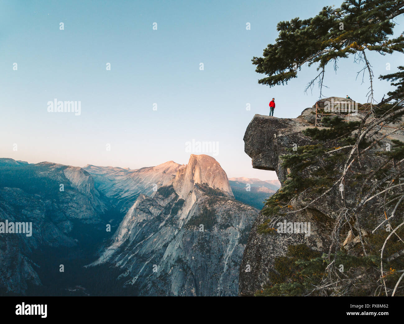 Eine furchtlose Wanderer steht auf einem überhängenden Felsen genießen den Blick auf die berühmten Half Dome am Glacier Point in schönen Abend dämmerung Blicken Stockfoto