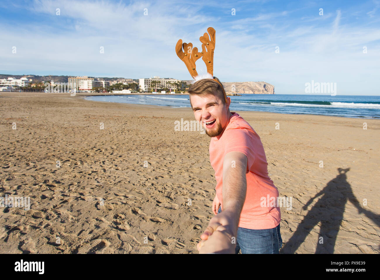 Folgen Sie mir, Ferien und Weihnachten Konzept-fröhlicher junger Mann mit Hirsch Hörner holding Santa's Hand am Strand. Stockfoto