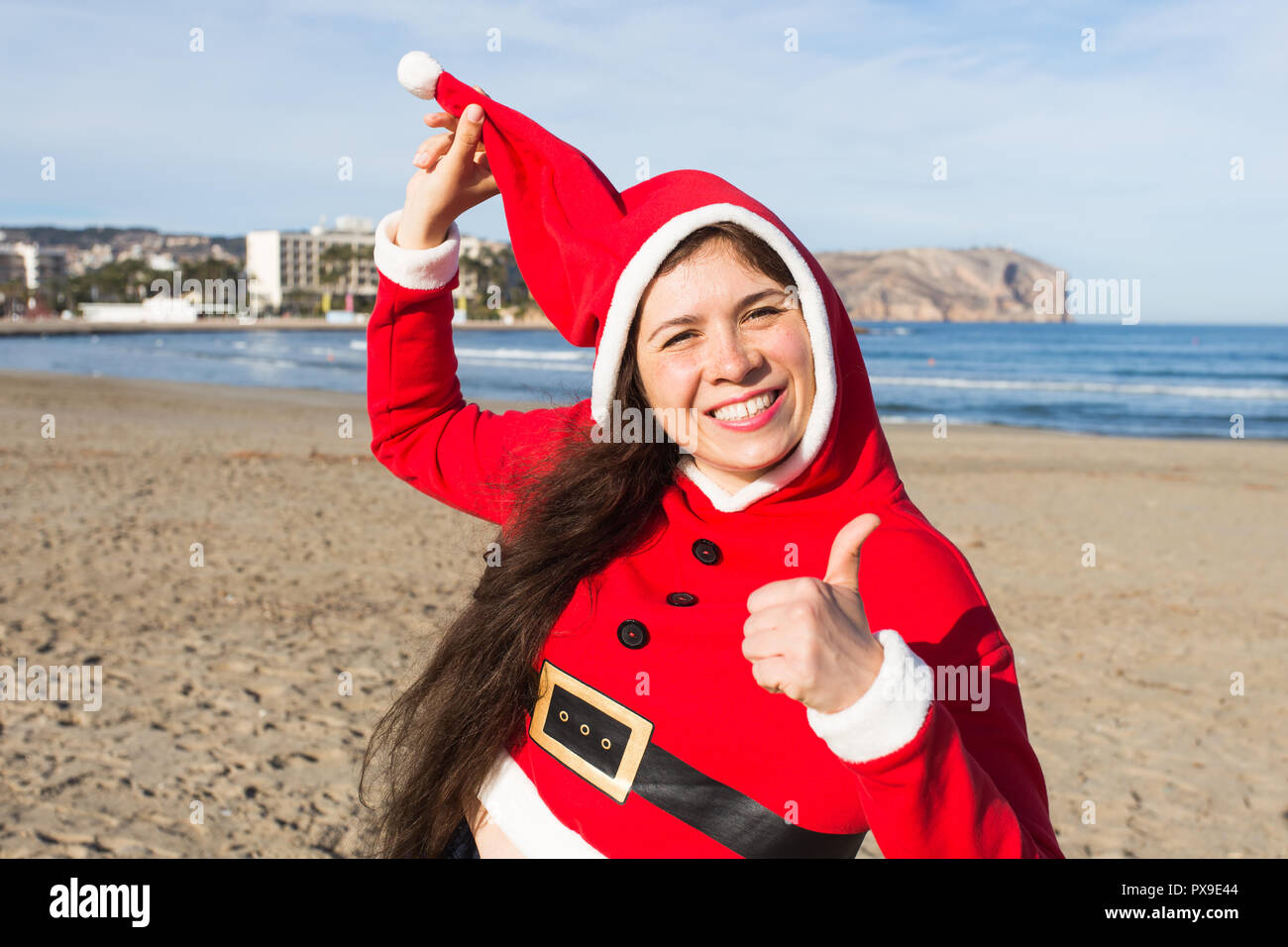 Weihnachts- und Urlaubsgeld Konzept - glückliche Frau in Santa Claus Kostüm mit Daumen hoch auf sandigen Strand Hintergrund Stockfoto