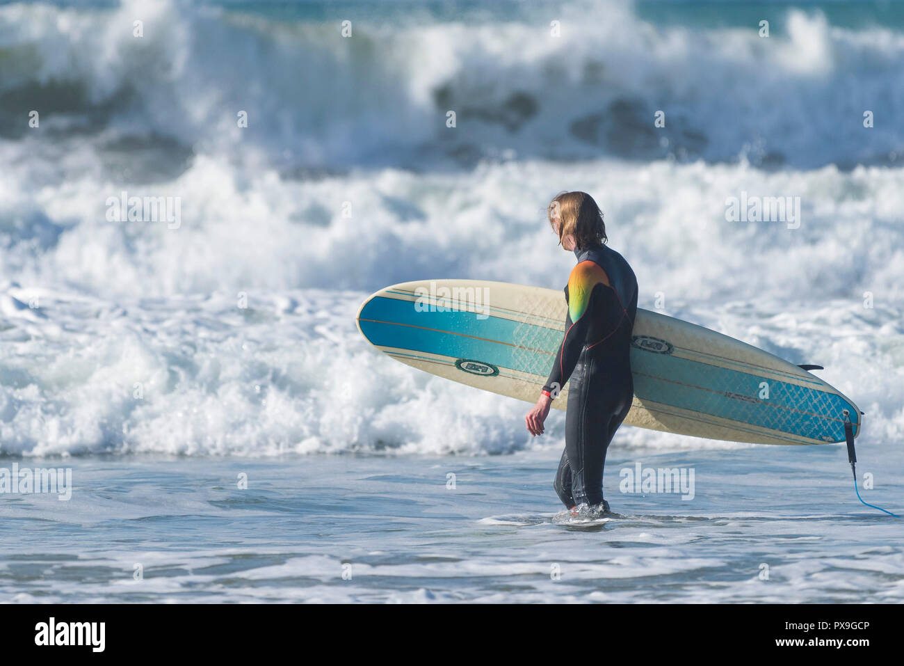 Surfen GROSSBRITANNIEN - ein Surfer sein Surfbrett tragen und wandern in das Meer bei Fistral in Newquay in Cornwall. Stockfoto