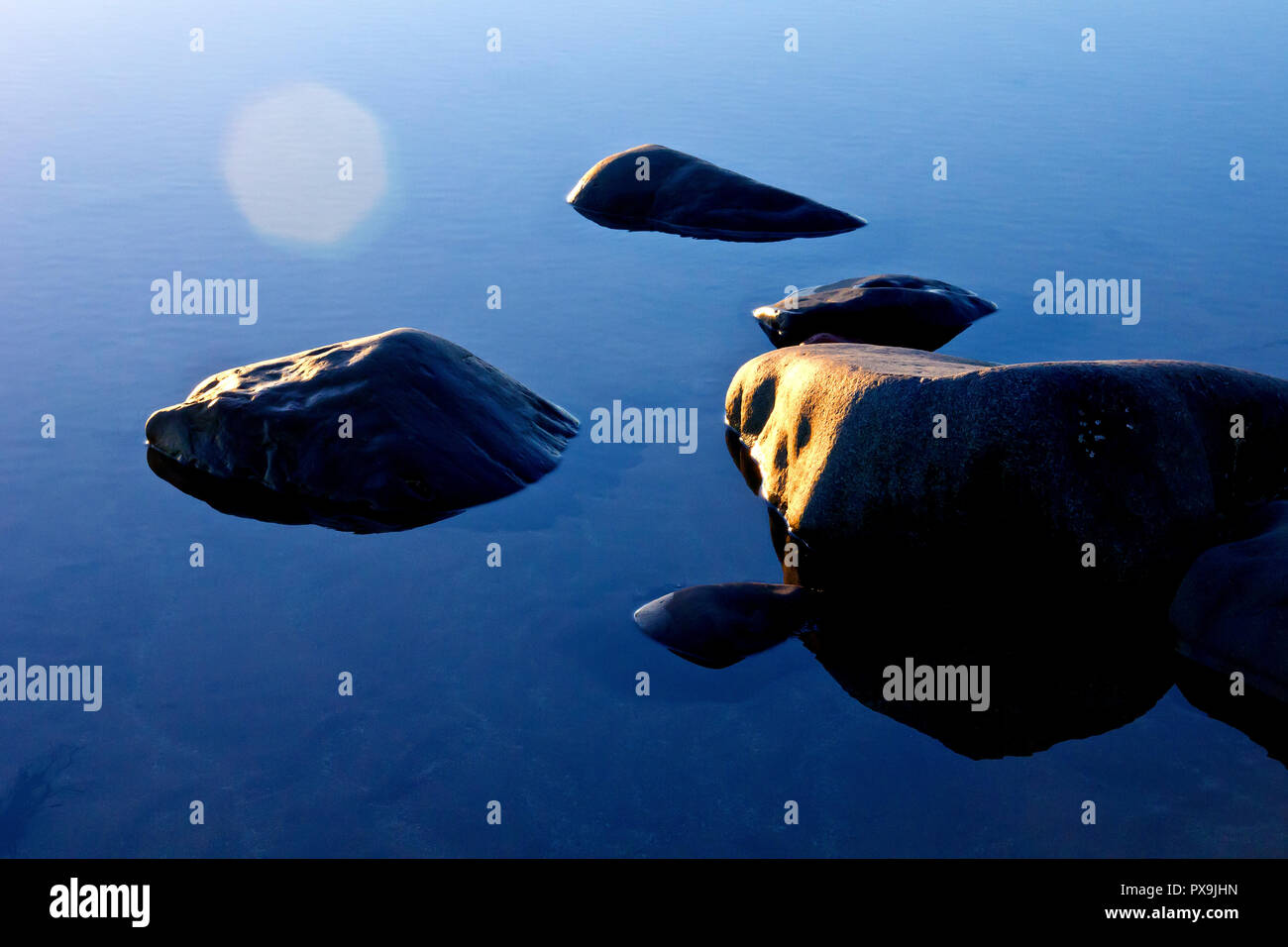 Felsen in einer ruhigen rockpool am Strand sitzen, beleuchtet durch eine niedrige Winter Sonne, so dass die optische Illusion der Felsen schwimmt auf dem Wasser. Stockfoto