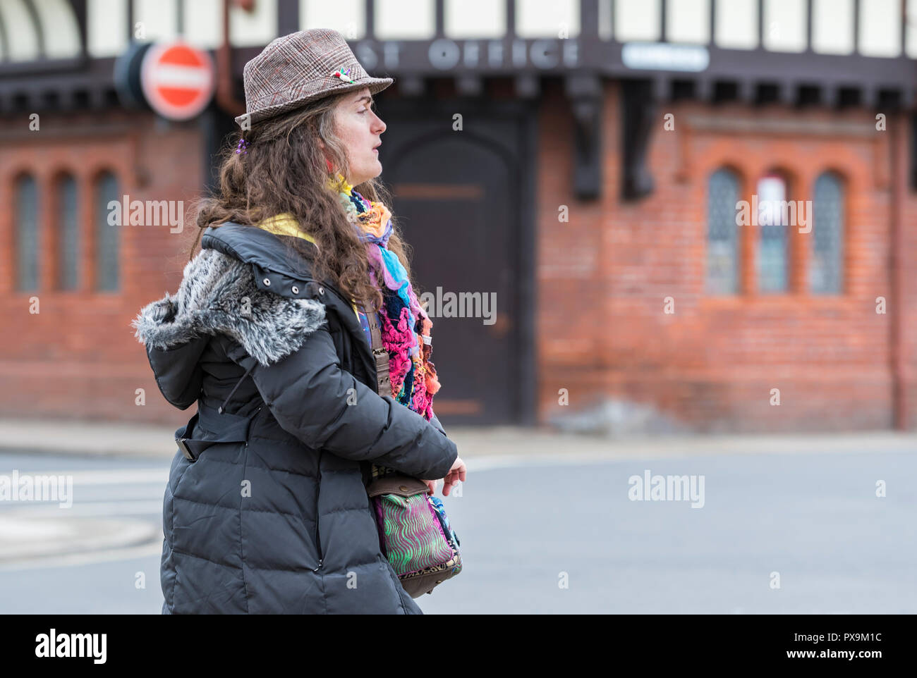 Seitliche Sicht auf eine Frau mittleren Alters zu Fuß warm tragen bunte Kleidung und einen Winter Mantel und Hut. Dame tragen bunte Kleidung. Stockfoto