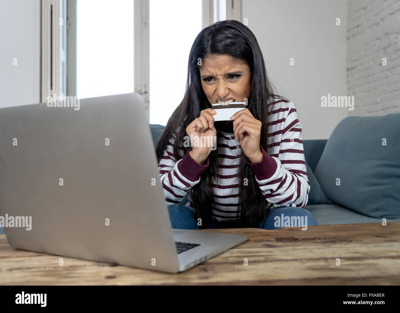 Attraktive junge Latin Frau verzweifelt und wütend mit Kreditkarte und Laptop Standortwahl auf dem Sofa zu Hause in der Kreditkarte Probleme Schulden online Zahlung online Stockfoto