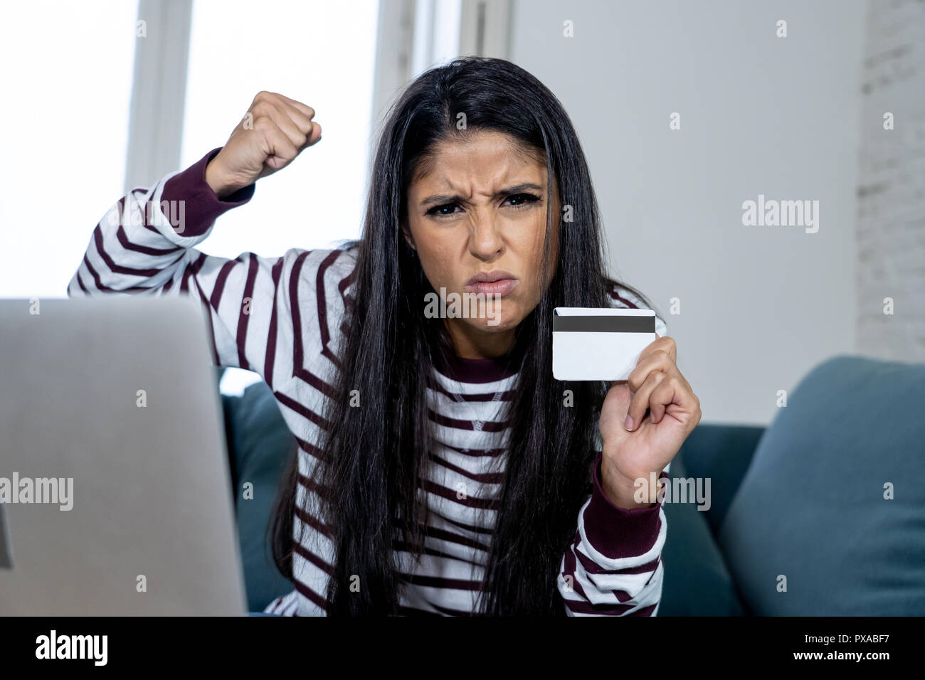 Attraktive junge Latin Frau verzweifelt und wütend mit Kreditkarte und Laptop Standortwahl auf dem Sofa zu Hause in der Kreditkarte Probleme Schulden online Zahlung online Stockfoto