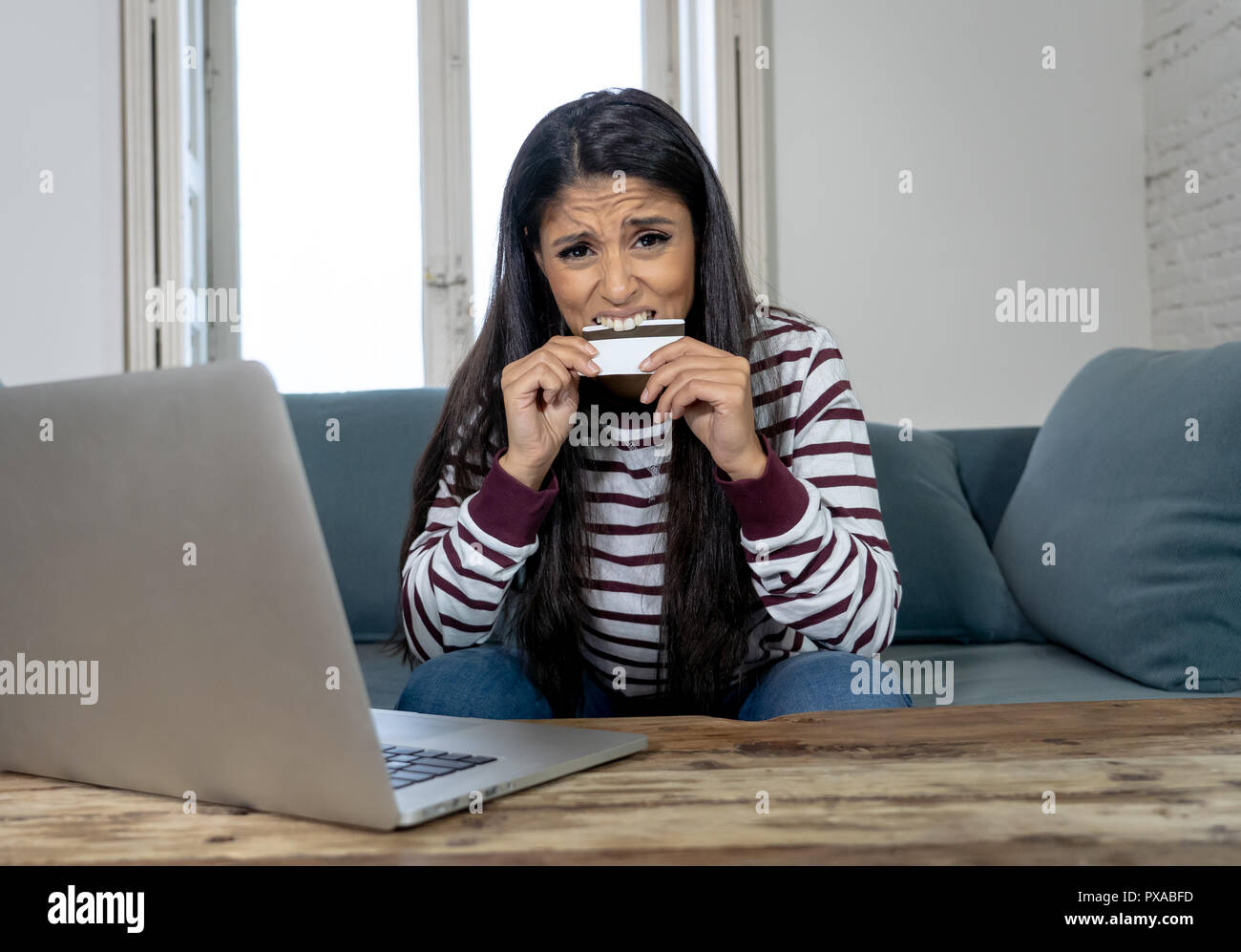 Attraktive junge Latin Frau verzweifelt und wütend mit Kreditkarte und Laptop Standortwahl auf dem Sofa zu Hause in der Kreditkarte Probleme Schulden online Zahlung online Stockfoto