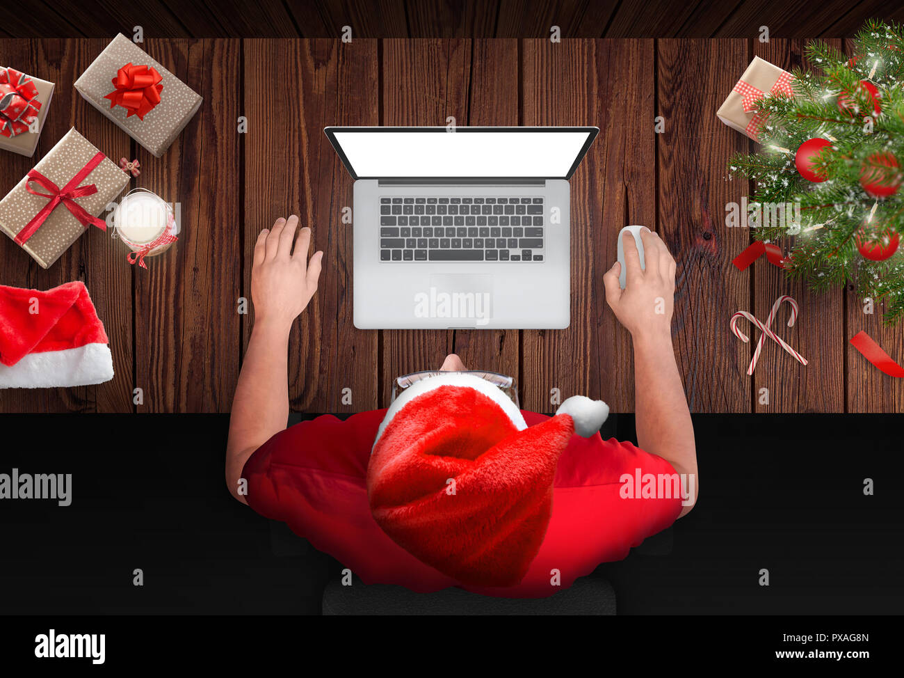 Mann mit Laptop während der Weihnachtsfeiertage. Weihnachtsbaum, Geschenke und Dekorationen neben. Draufsicht auf die Szene. Stockfoto