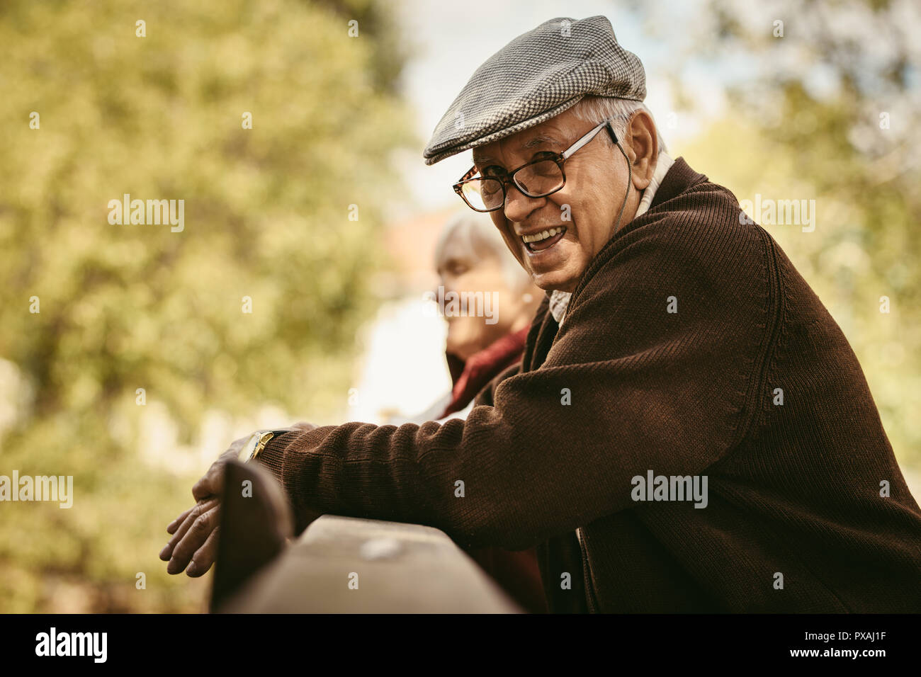Portrait von Happy älterer Mann mit Brille und Deckel von einem holzgeländer mit einer Frau an der zurück in die PARK-Stellung. Lächelnd alter Mann im Park auf einem Winte Stockfoto