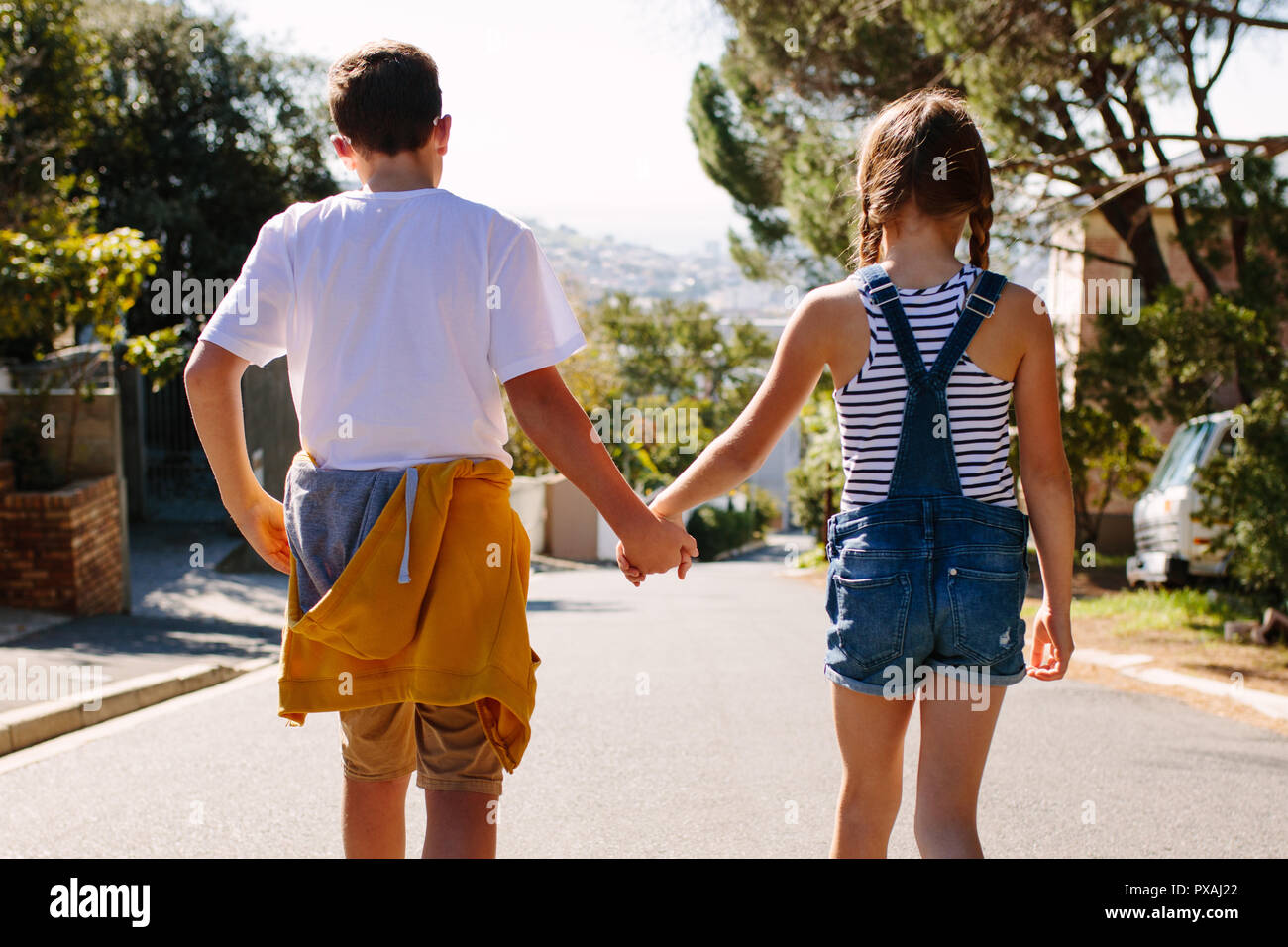 Kinder in der Liebe zu Fuß auf einer Straße, die Hand in Hand an einem sonnigen Tag. Junge und Mädchen zu Fuß auf einer verlassenen Straße zusammen. Stockfoto