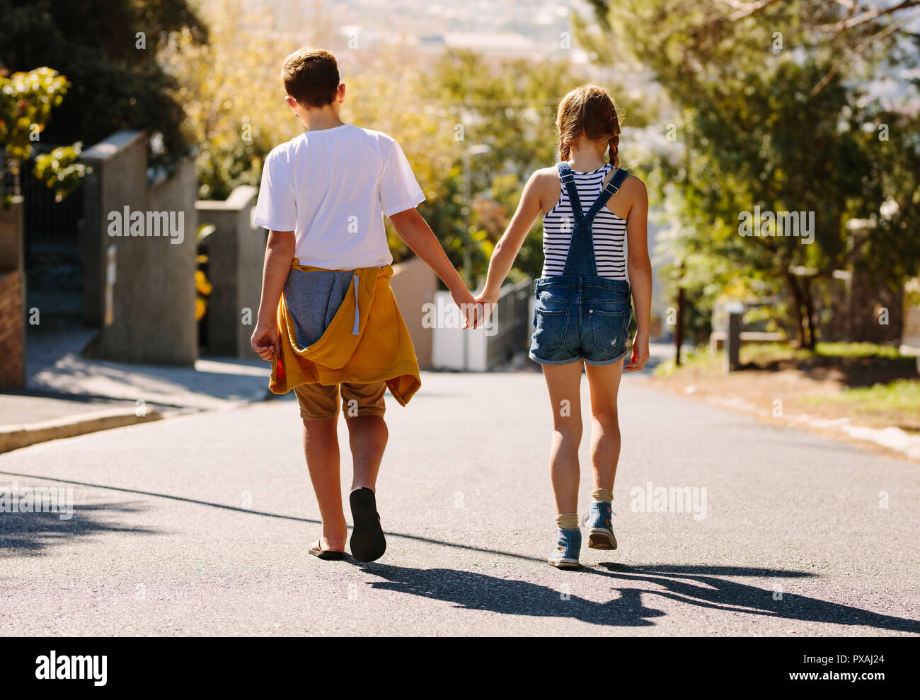 Junge und Mädchen gehen auf eine leere Straße zusammen. Kinder in der Liebe zu Fuß auf einer Straße, die Hand in Hand an einem sonnigen Tag. Stockfoto