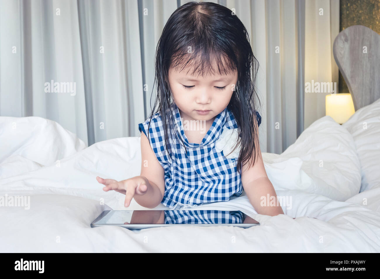 Kleines Mädchen auf dem Bett liegend mit Tablet glücklich lächelnd über das Internet ansehen und Spaß haben, in Beziehung mit Technologie Konzept Stockfoto