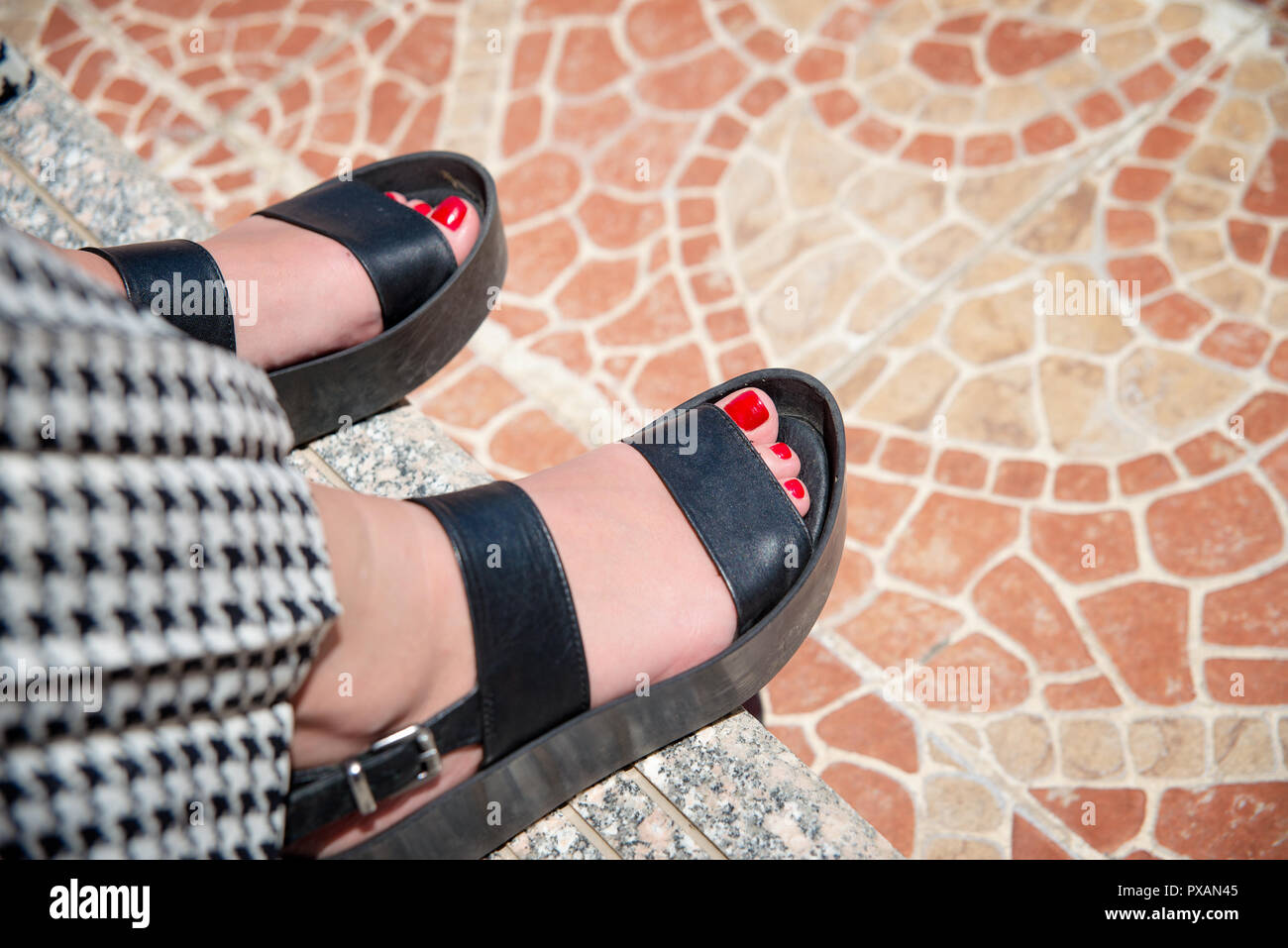 Weibliche Füße in schwarzen Sandaletten Stockfoto