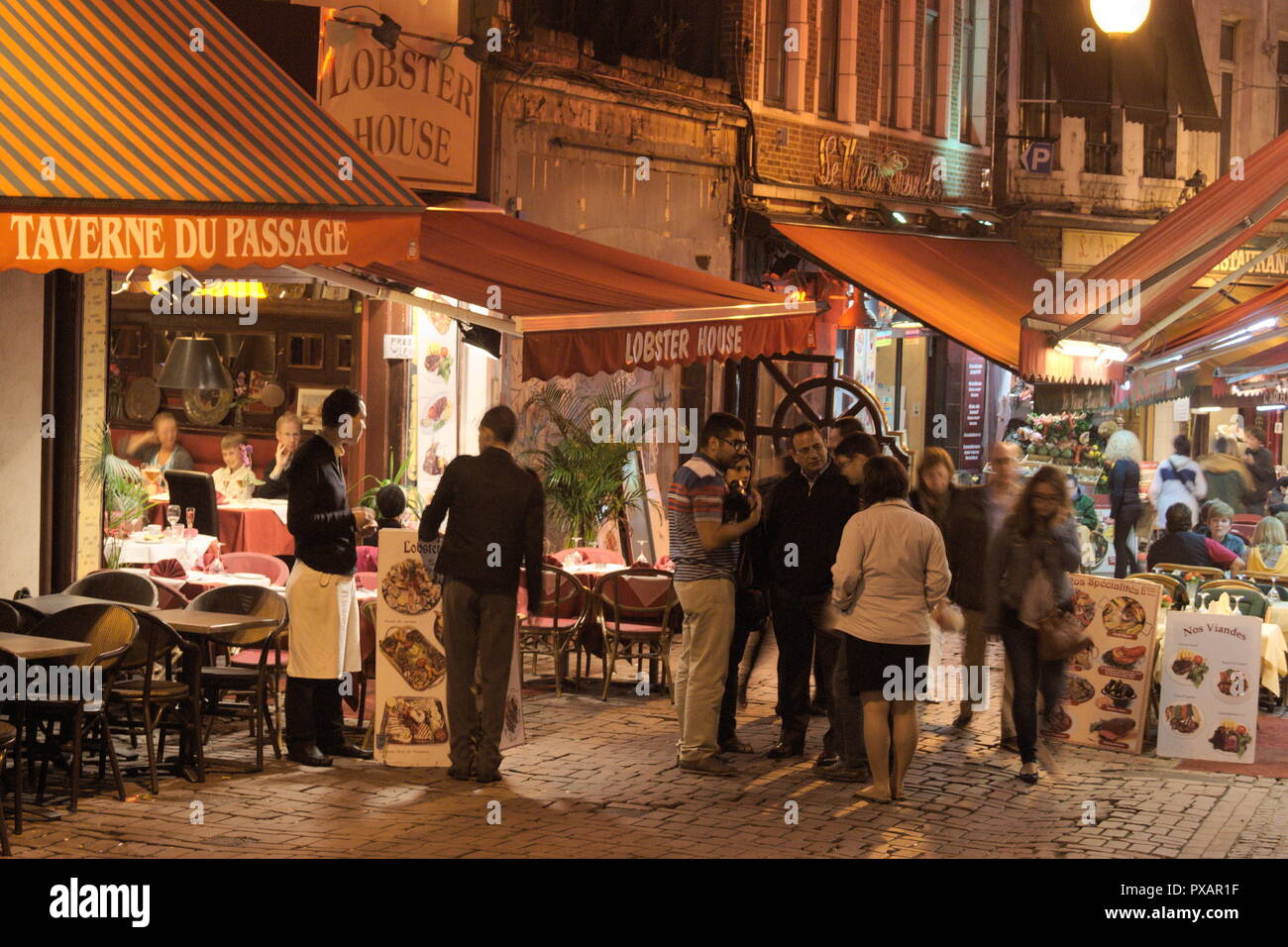 Nachtaufnahme im Herzen der historischen Stadt Brüssel. Restaurants, Cafés und Bistros säumen den Straßenbelag, während die Gäste ihr Essen genießen. Stockfoto