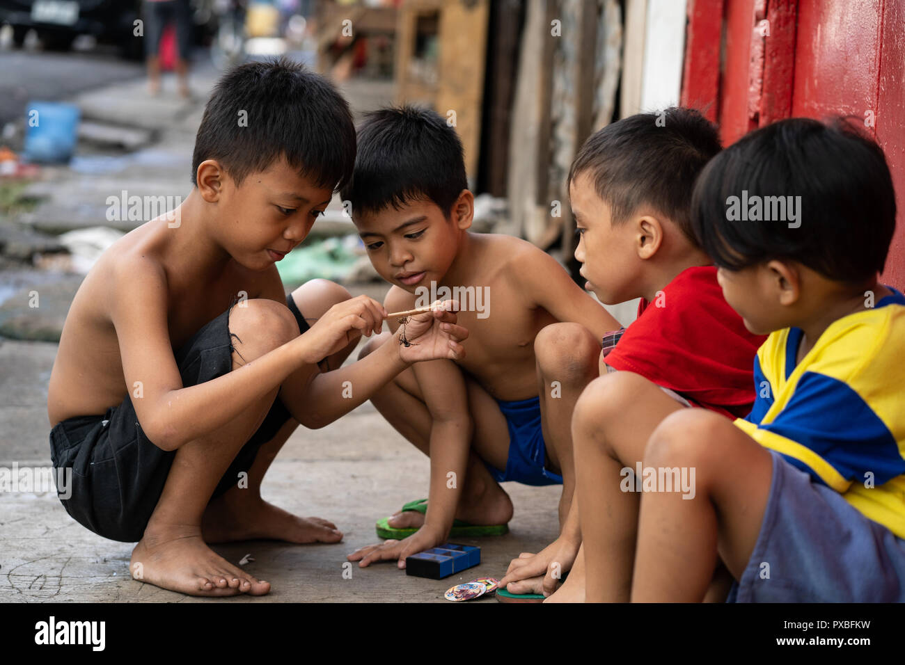 Jungen auf einem Bürgersteig spielen das Spiel des Spider kämpfen, beliebt bei jungen Kindern auf den Philippinen Stockfoto