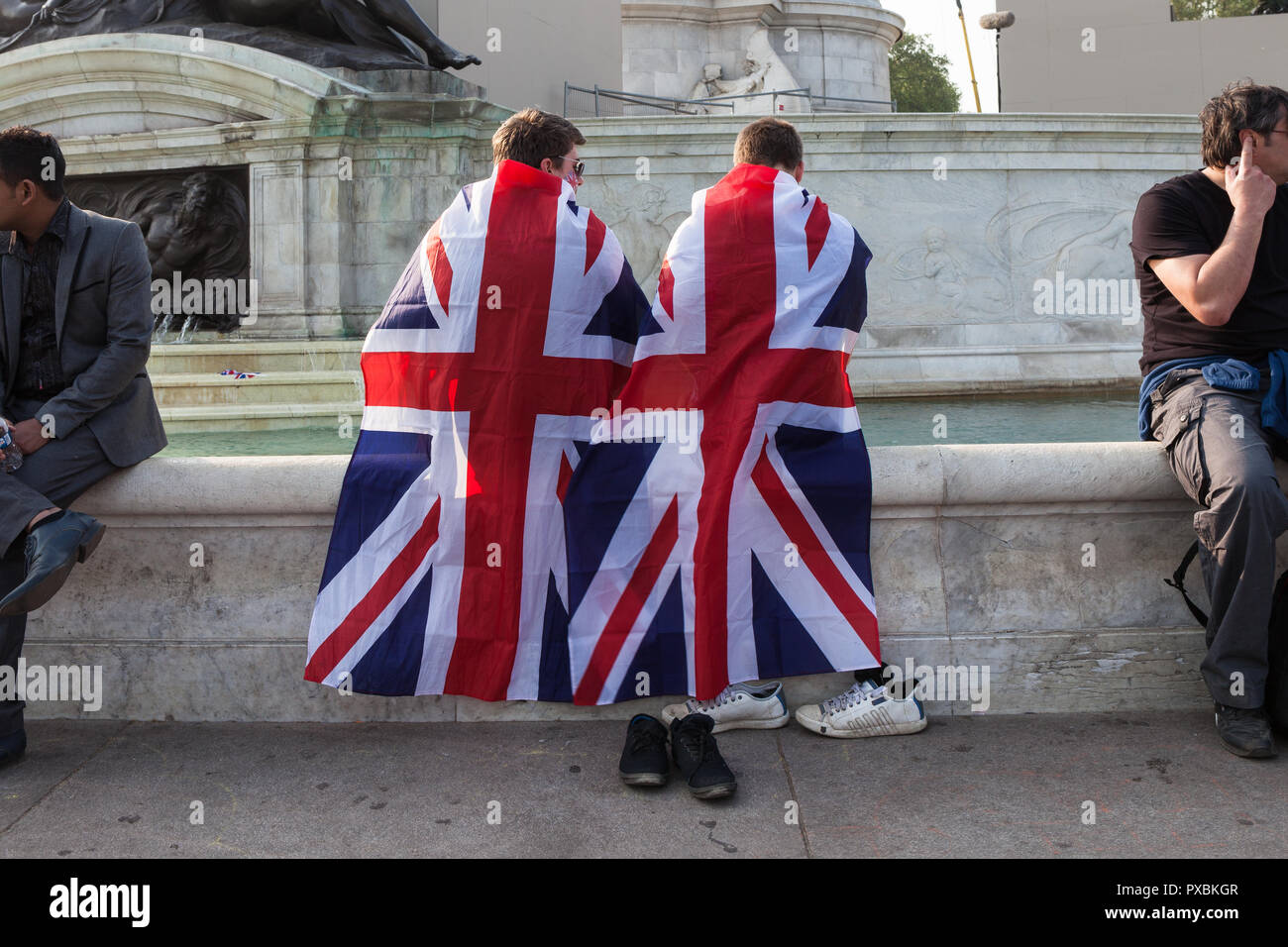 Zwei junge Männer in Union Jack Fahnen eingewickelt und kühlen ihre Füße im Brunnen vor dem Buckingham Palace. Stockfoto