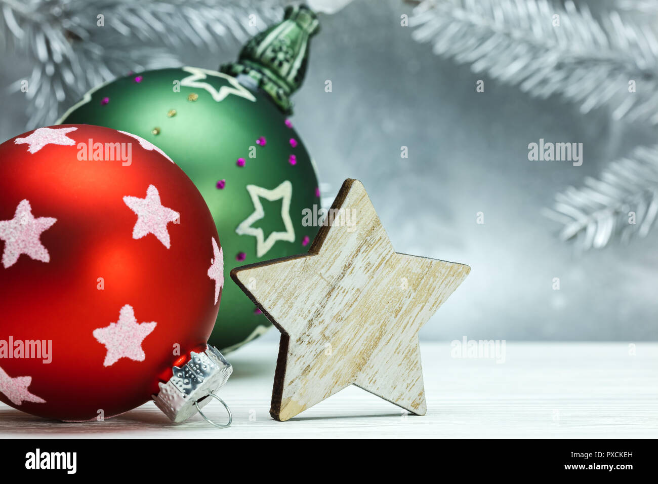 Rote und Grüne Weihnachten Kugeln und Holz- dekorative Stern auf unscharfen Silberner Hintergrund mit Tannenbaum Äste Stockfoto