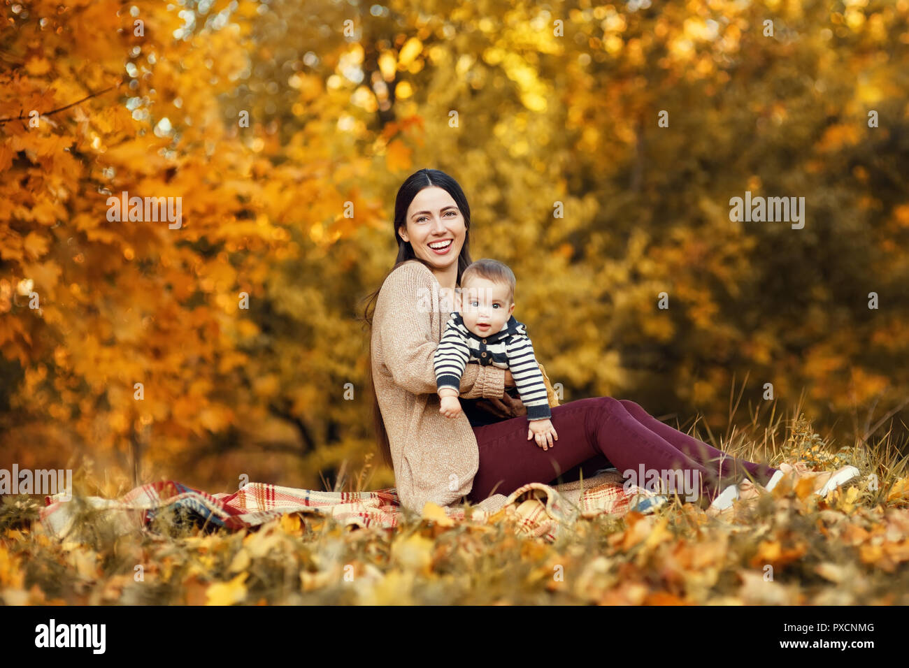 Fröhliche Mutter mit Baby Junge spielt im Herbst Park. Schöne Frau ihren kleinen Sohn im Freien Holding Stockfoto