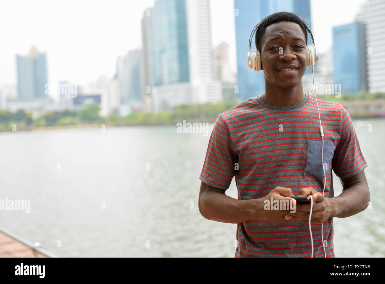 Afrikanischer Mann im Park mit Handy und Musik hören mit Kopfhörern Stockfoto