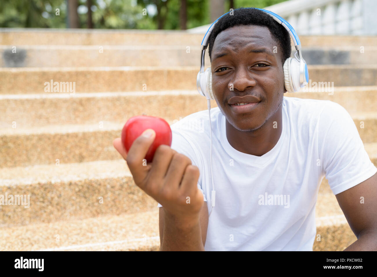 Afrikanischer Mann Musik hören mit Kopfhörern und holding red apple Stockfoto