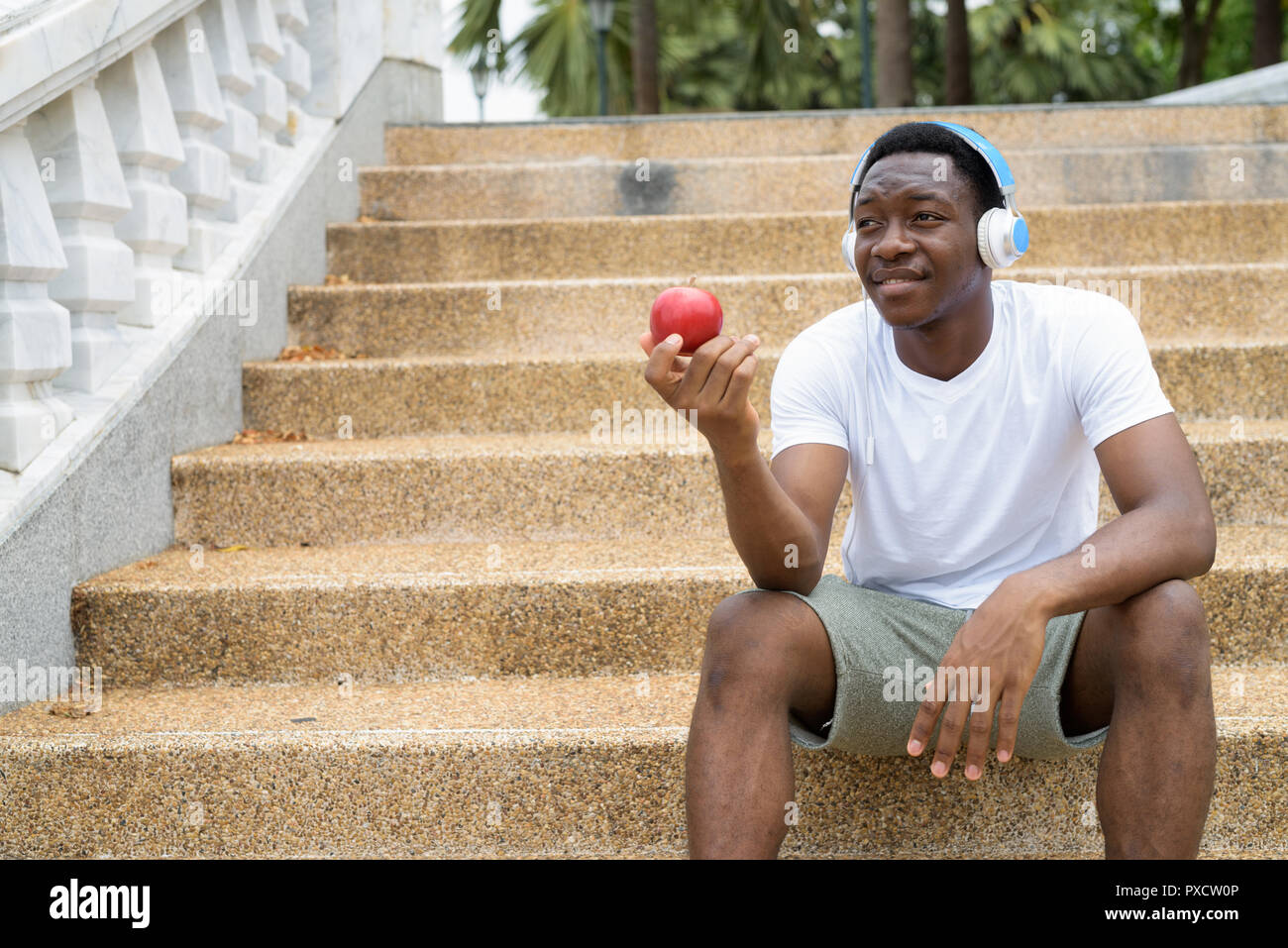 Afrikanischer Mann Musik hören mit Kopfhörern und holding red apple Stockfoto